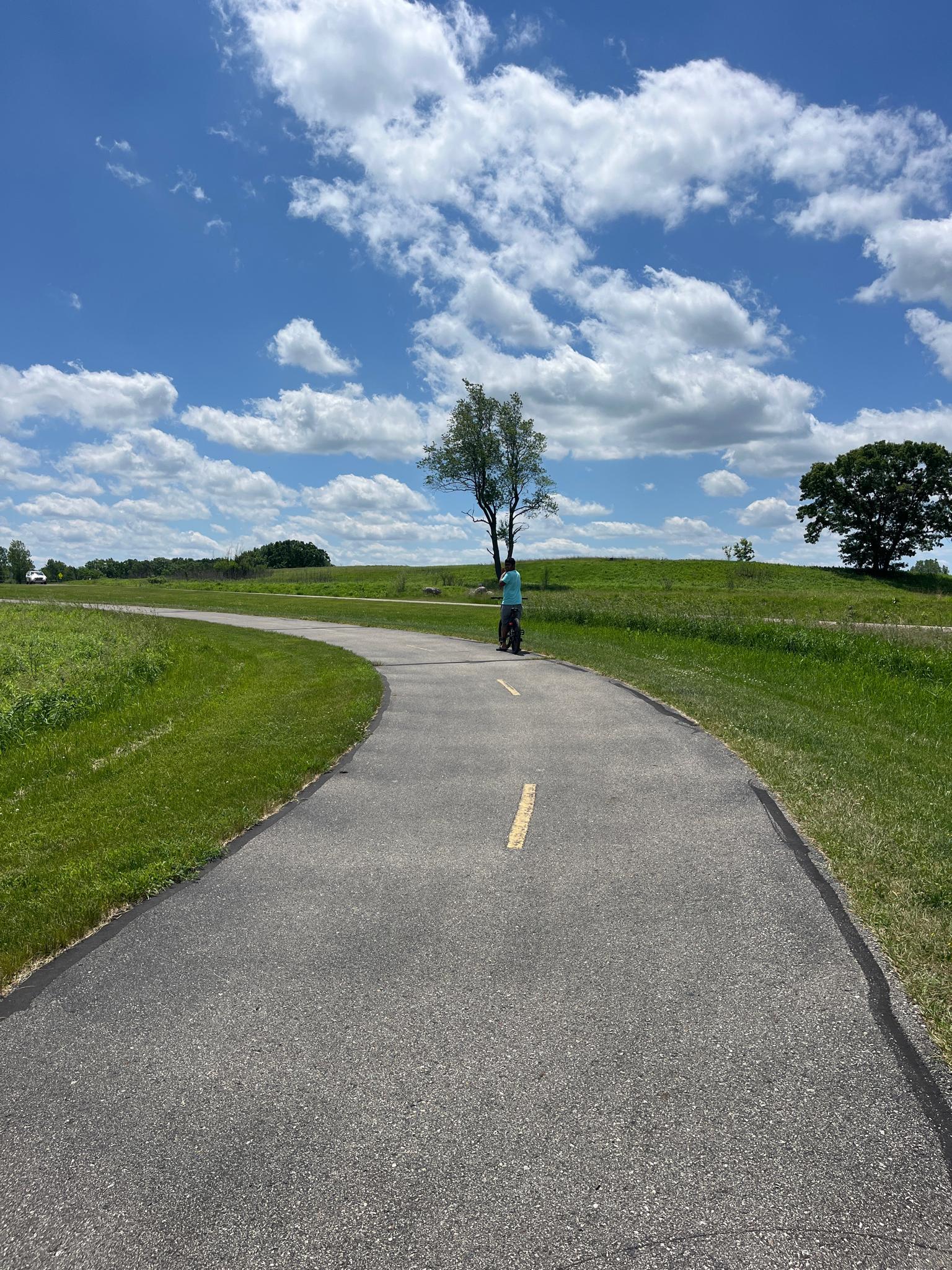 Person on bike on winding paved path through sunny green hills.