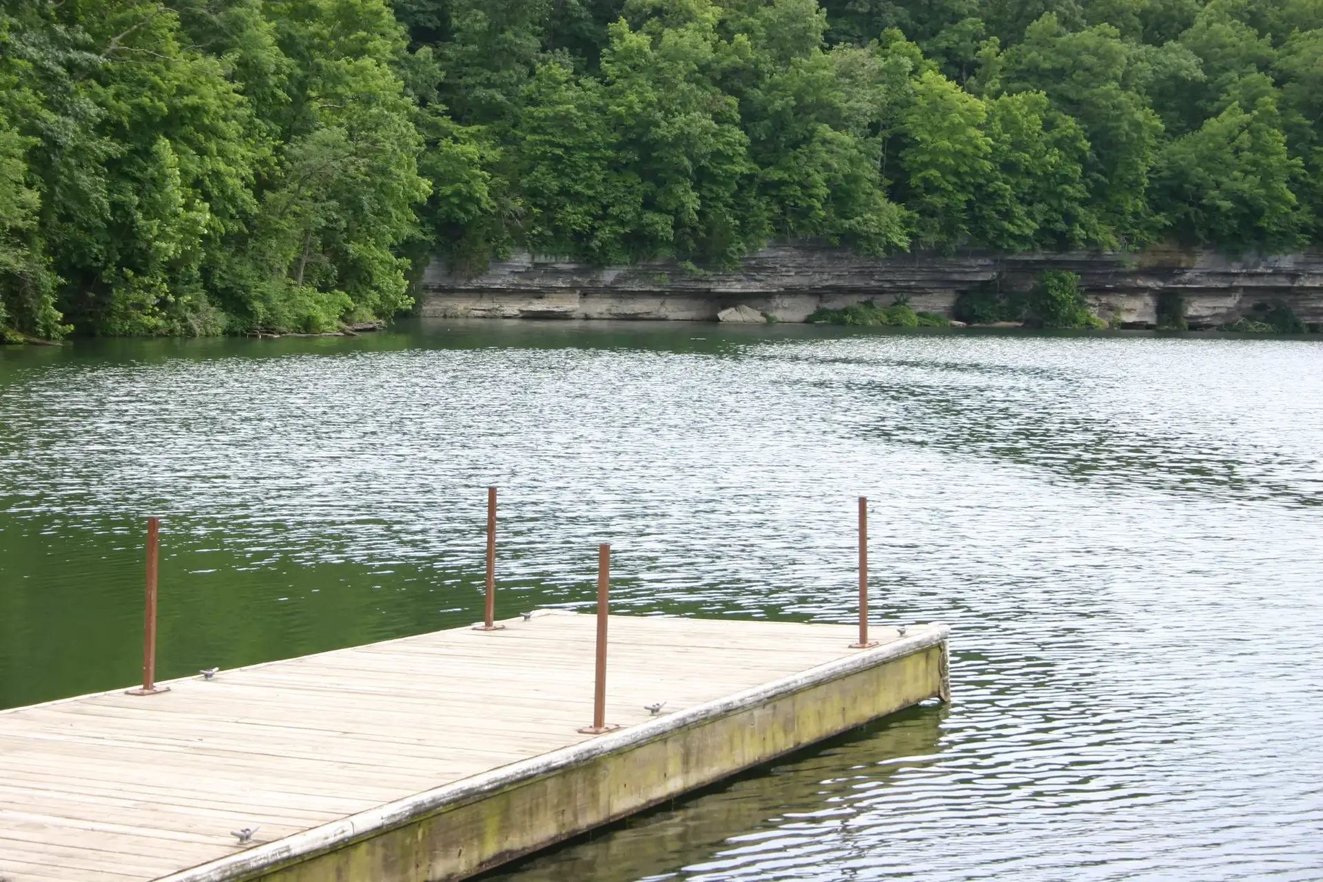 Empty wooden dock extends into a calm lake surrounded by green forest.