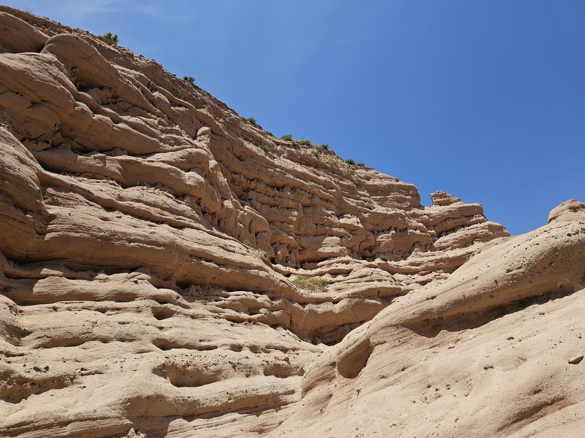 Close-up of layered, eroded sandstone cliffs under a bright blue sky.