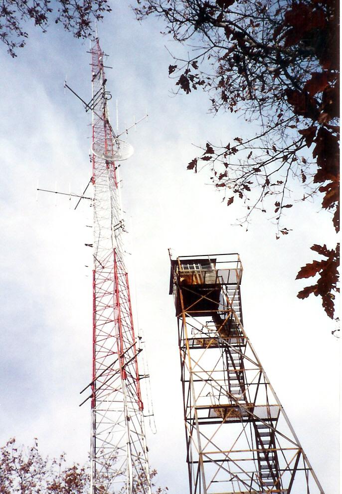 A tall red and white communication tower next to a shorter observation tower.