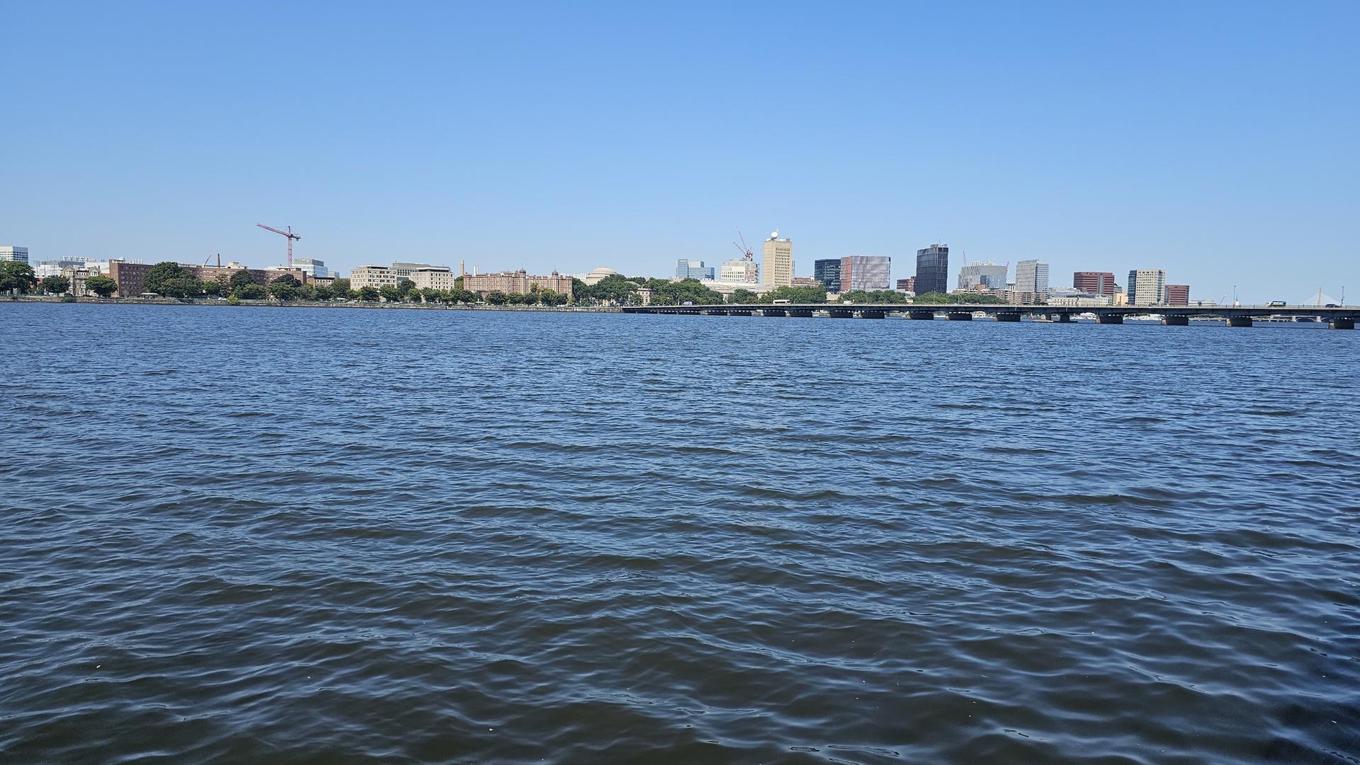Wide river with a distant city skyline and bridge under a clear blue sky.