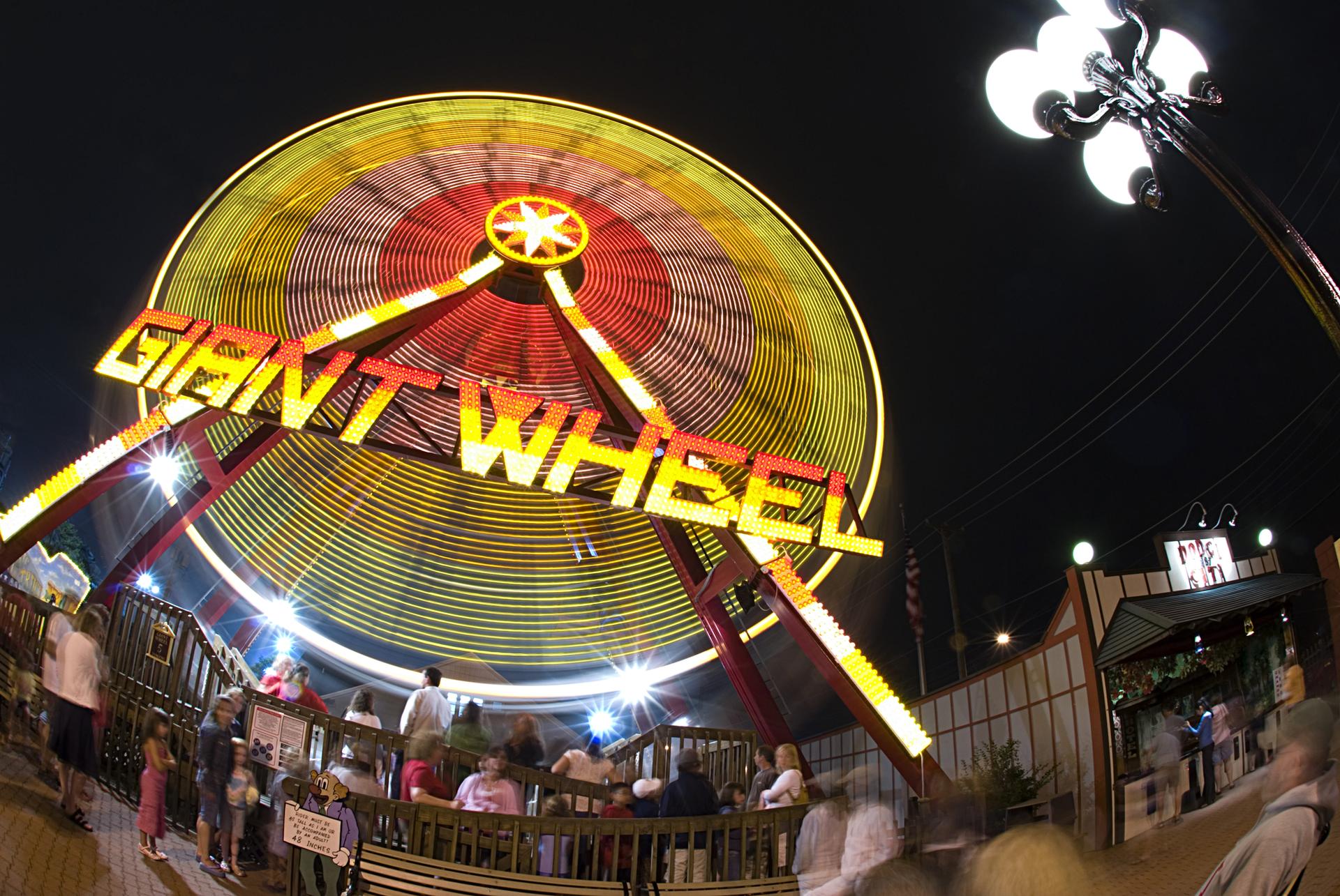 Brightly lit amusement park ride with people at night, motion blur.