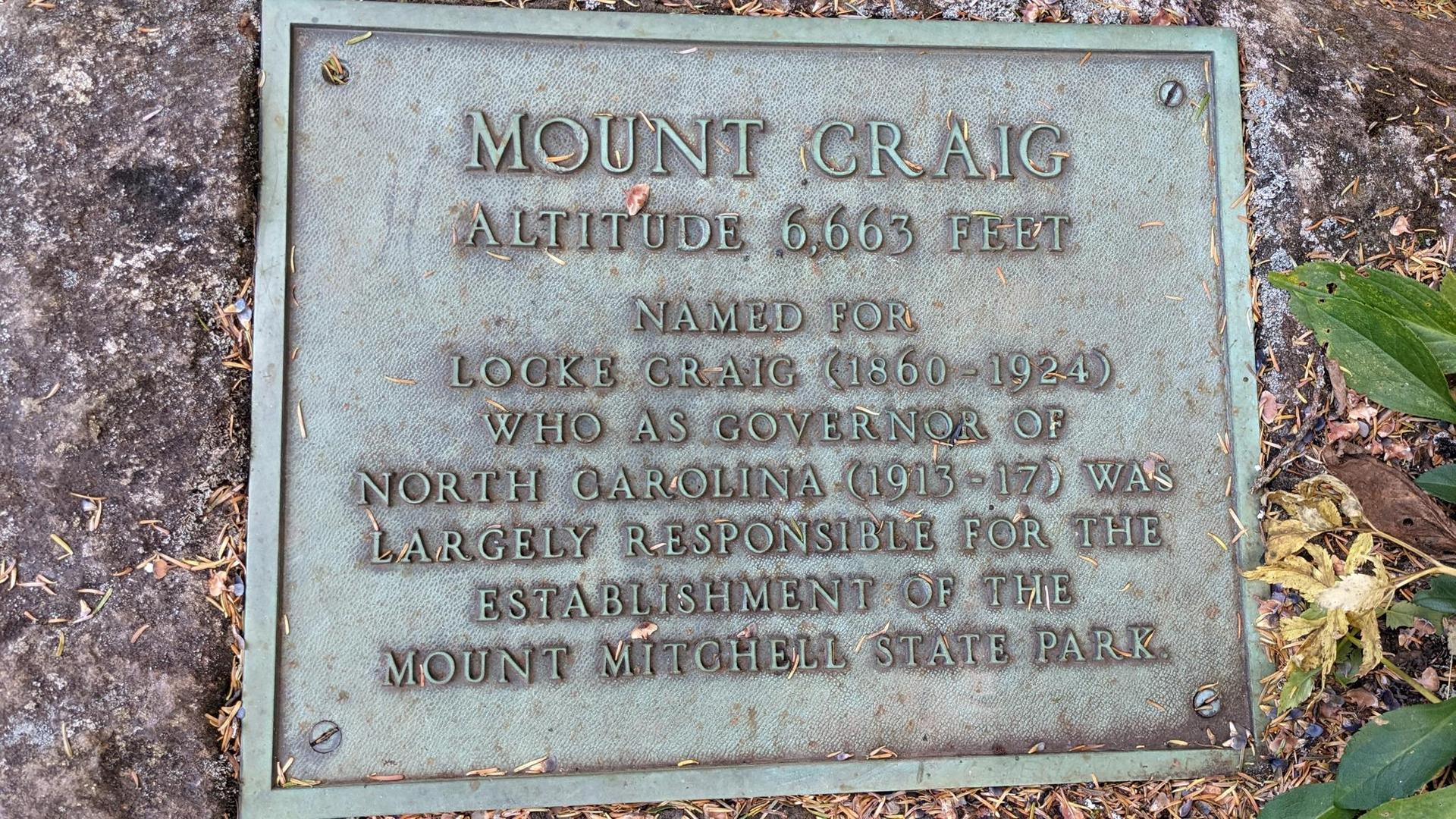 A weathered bronze plaque on a rock, detailing historical information.
