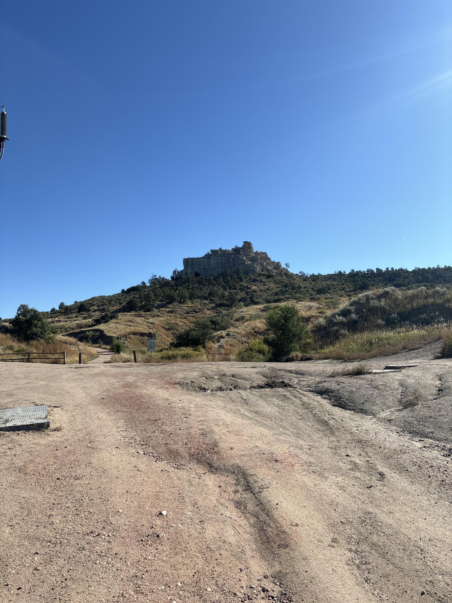 Wide dirt road leading towards a large rock formation on a sunny day.