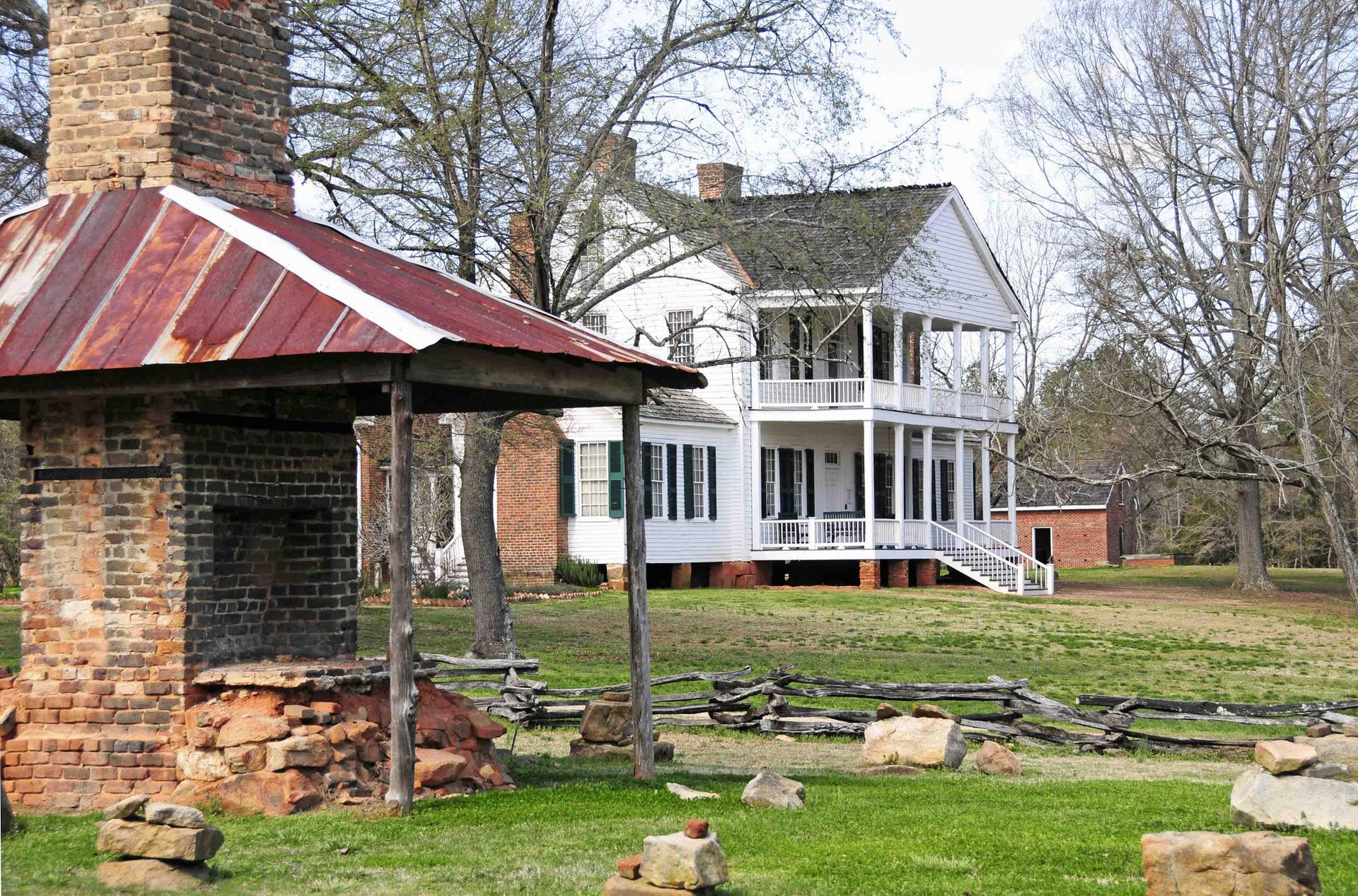 White historic house with double porch behind a brick outdoor fireplace.