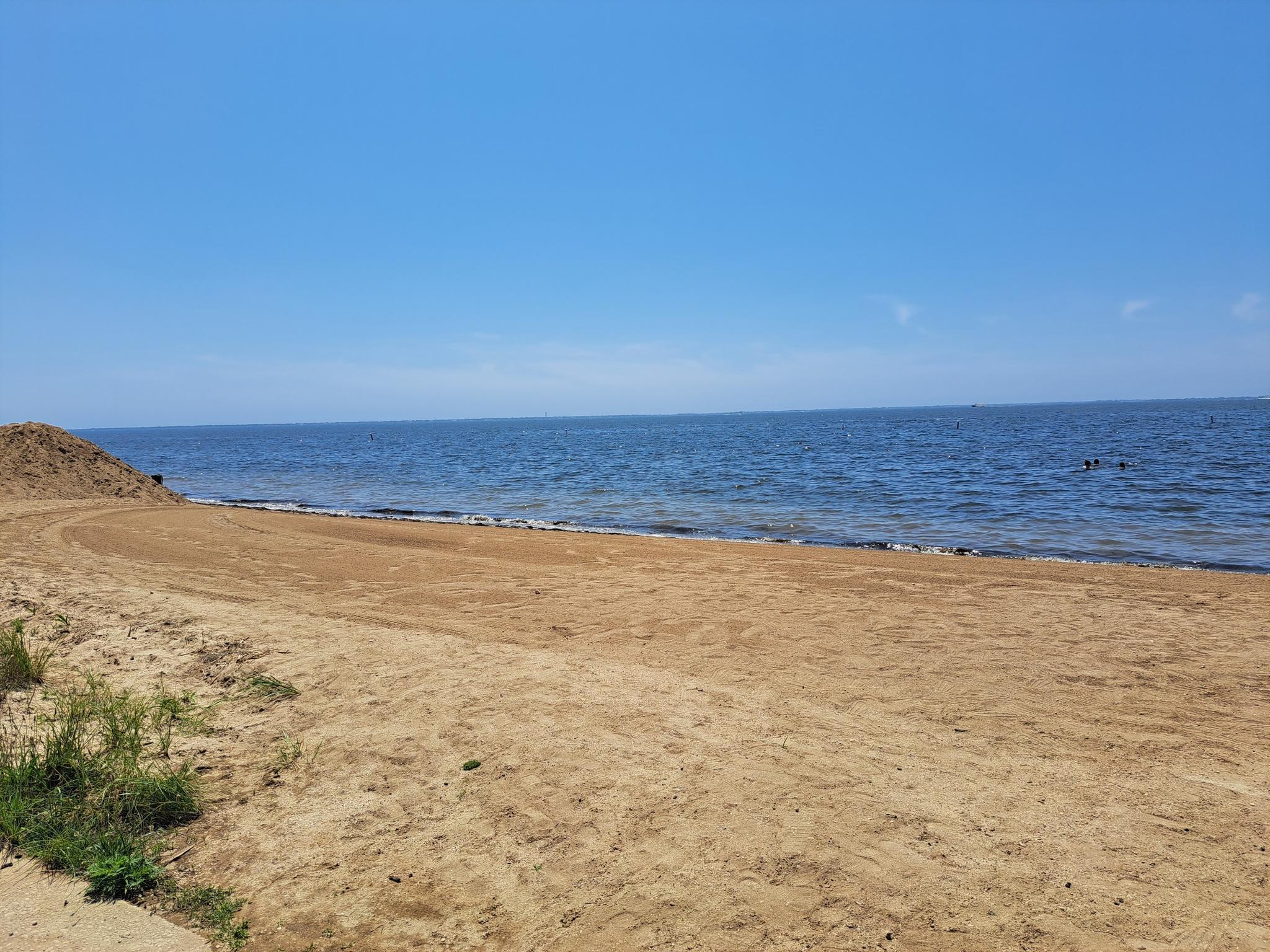 Expansive sandy beach meets calm blue ocean under a bright, clear sky.