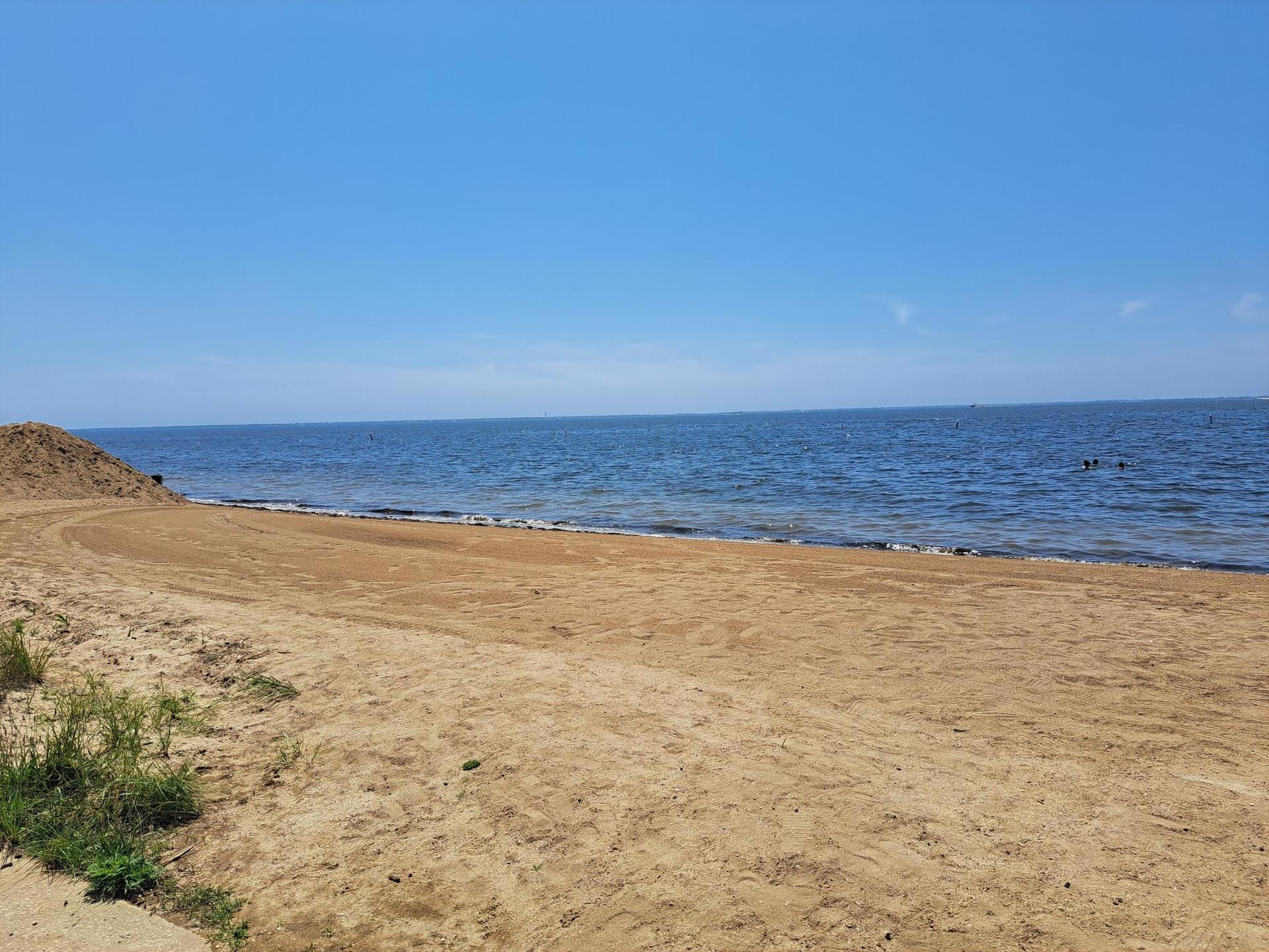 Expansive sandy beach meets calm blue ocean under a bright, clear sky.