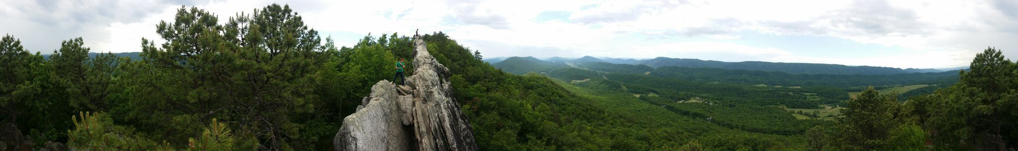 Panoramic view of a rocky ridge overlooking lush green mountains under cloudy skies.