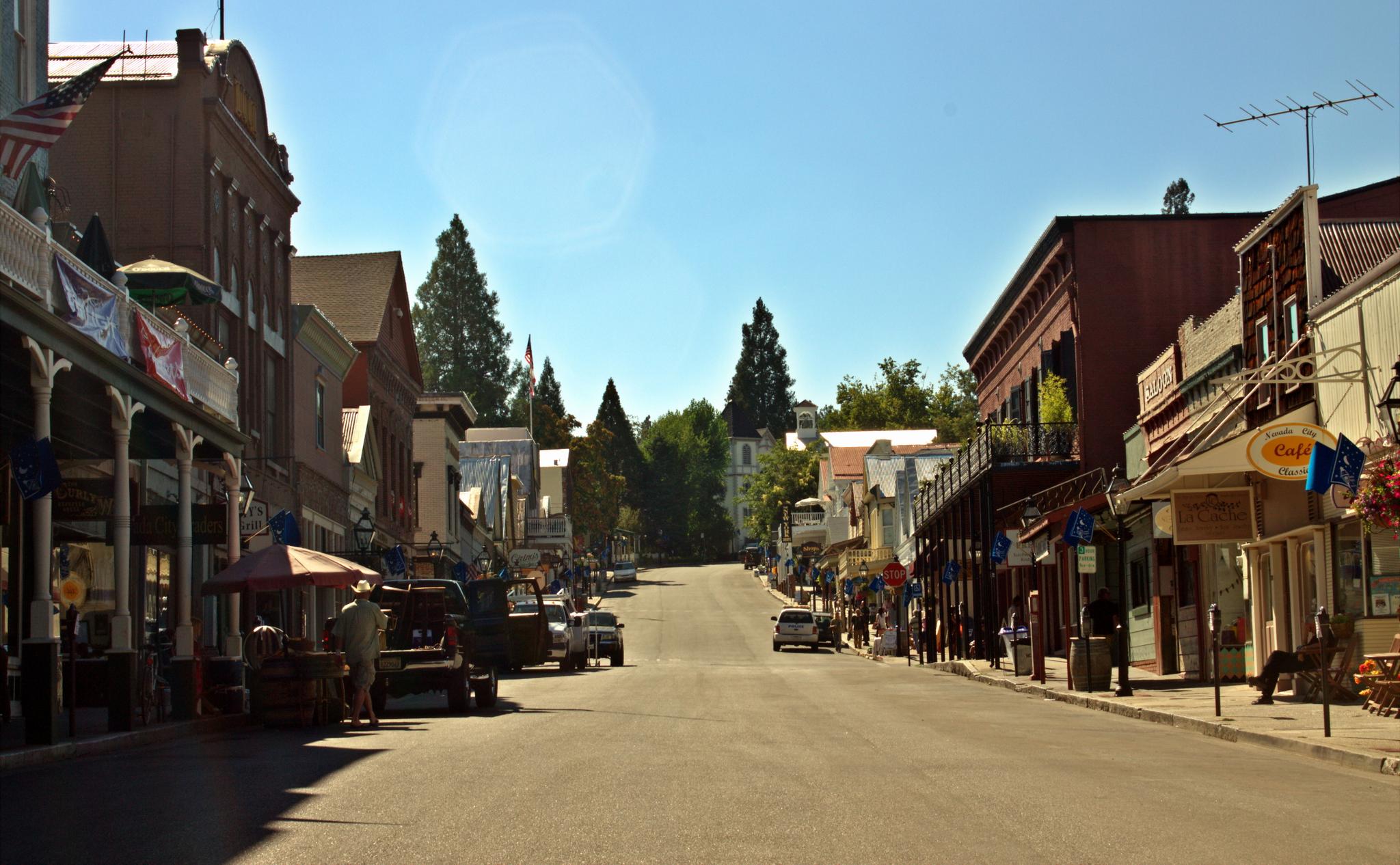 A sunny, wide street lined with historic buildings and a few people.
