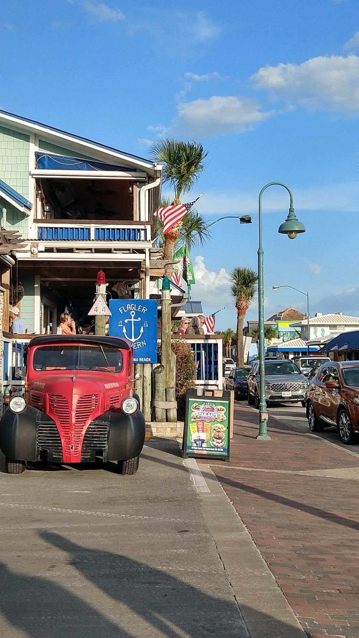 Red vintage truck parked on a sunny street with buildings and palm trees. - New Smyrna Beach loop