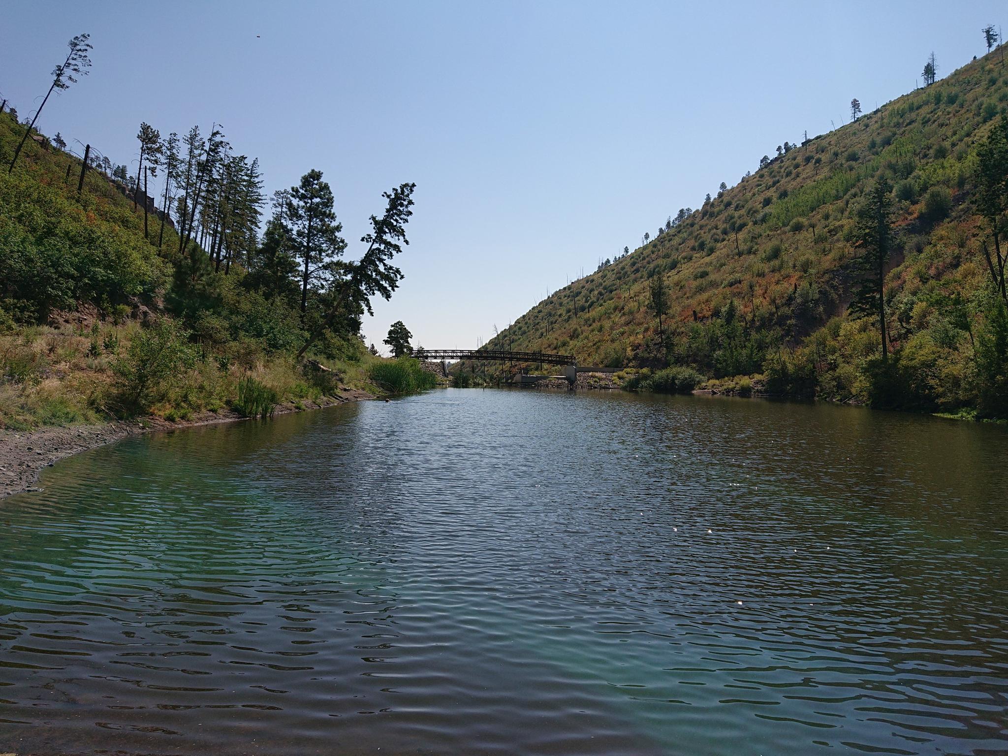 A calm river flows between green, tree-covered hills under a clear sky.