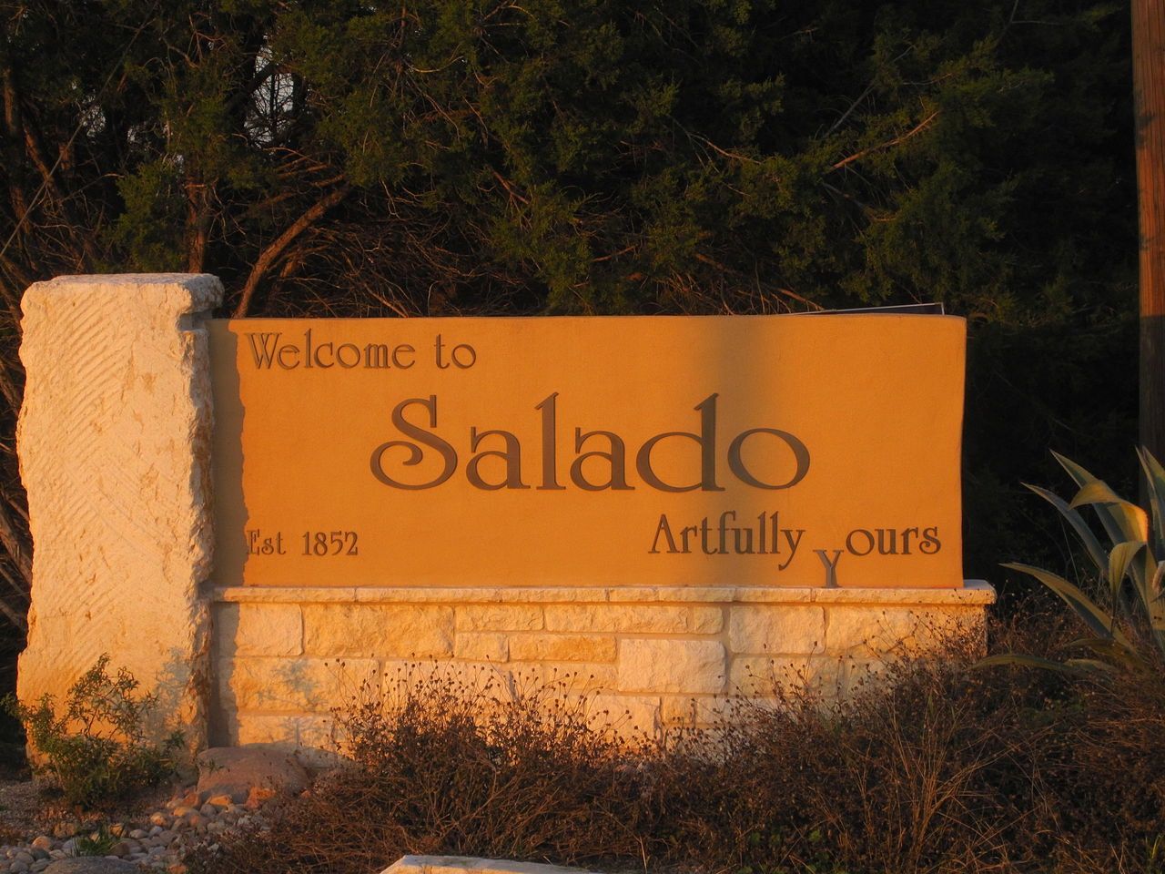 A stone and stucco welcome sign bathed in warm golden light. - Salado loop