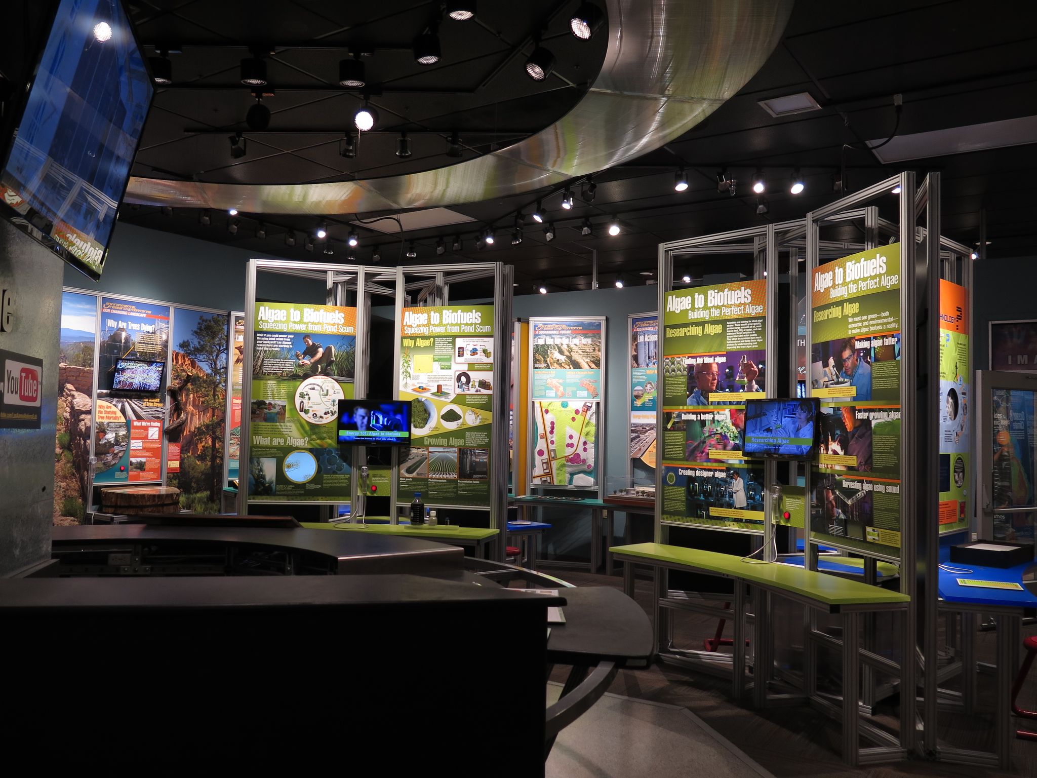 Indoor exhibit hall with multiple screens, informational panels, and bright overhead lights. - Bradbury Science Museum – Los Alamos Valley loop from Route 2/12 @ Rover