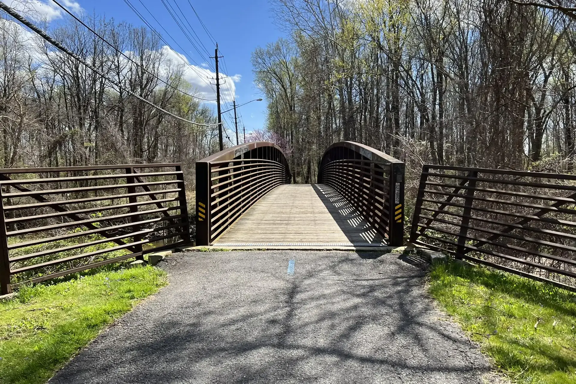 A brown arched pedestrian bridge spans a path on a sunny day.