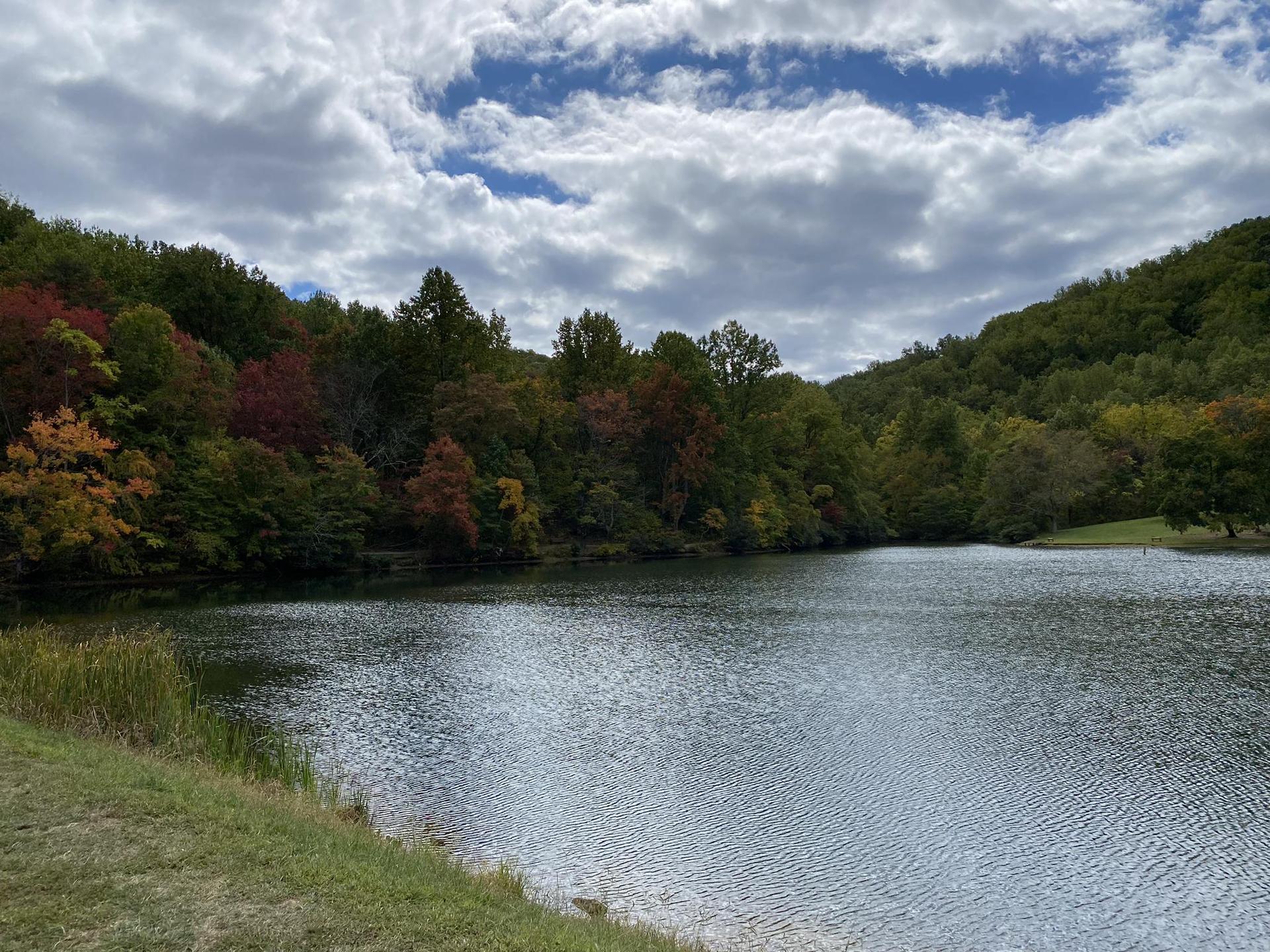 A lake surrounded by hills with colorful autumn trees under a cloudy sky.