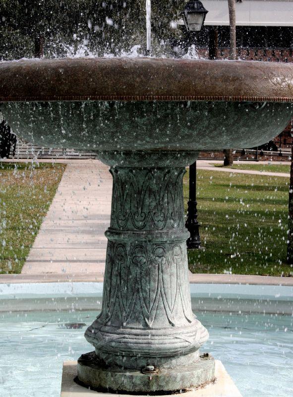Ornate stone fountain splashing water on a sunny day with green grass.