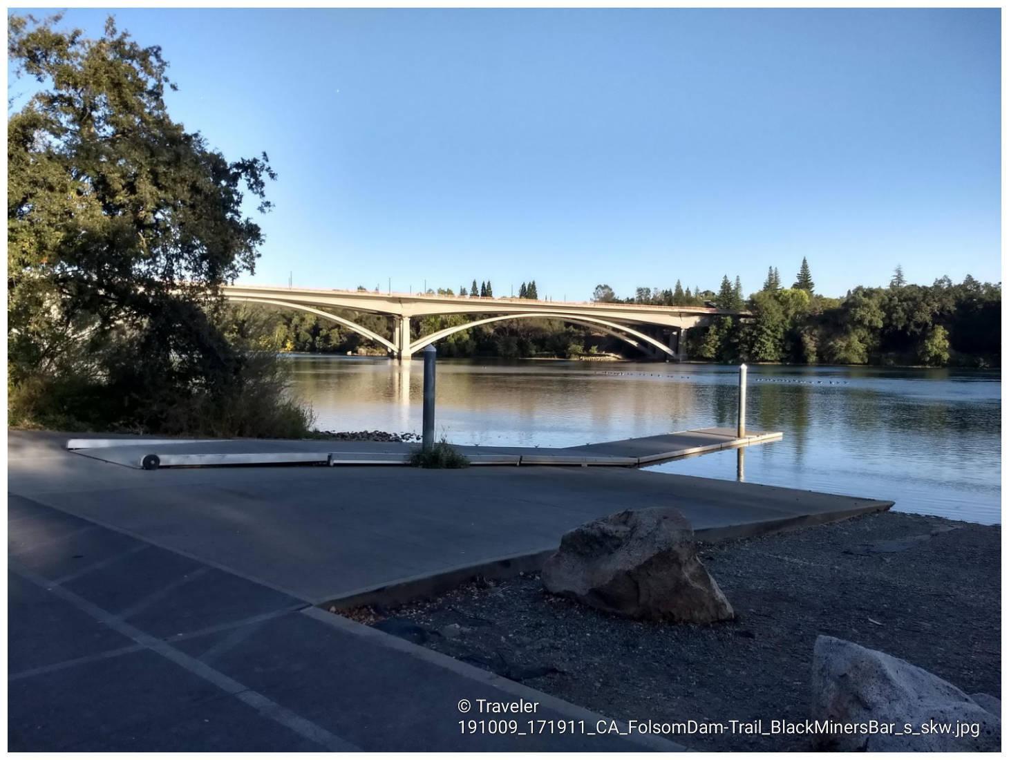 Paved boat ramp leading to calm water with a large arch bridge.