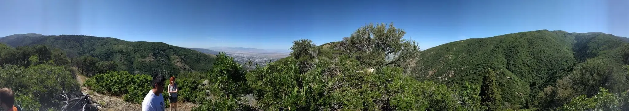Two people on a sunny mountain overlook, viewing green hills and a hazy valley. - Parrish Creek Trail