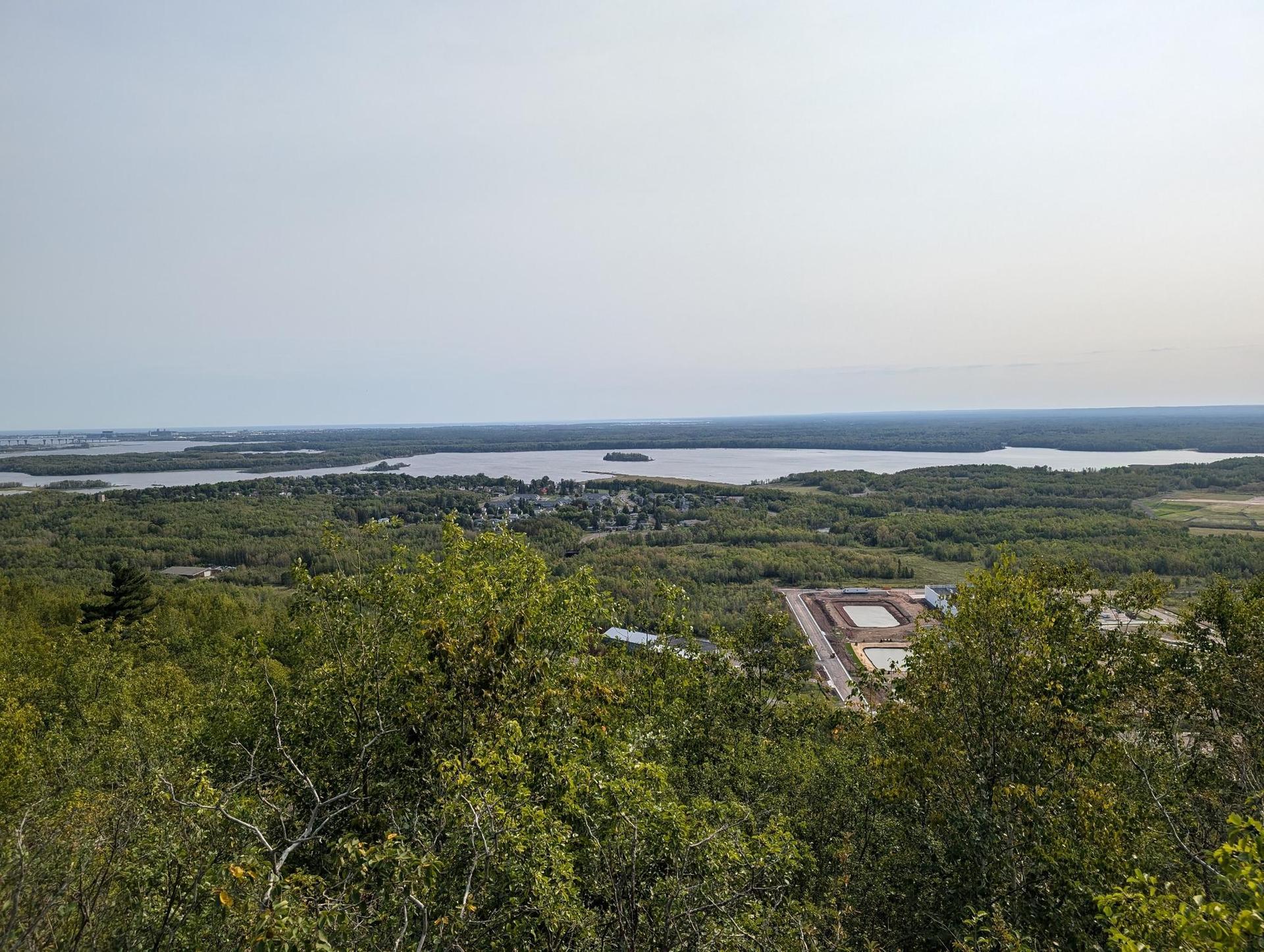 Overlook of a large lake and forested landscape under a hazy sky.
