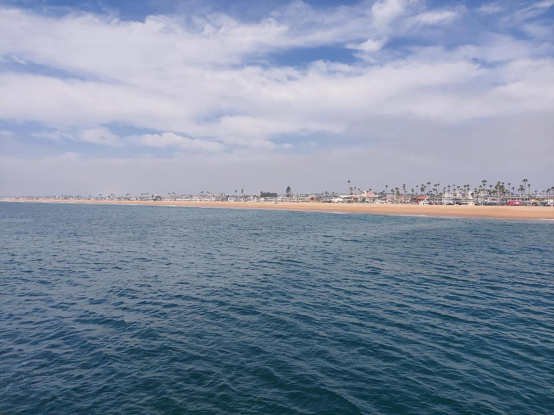 Wide view of blue ocean next to a long, sandy beach.