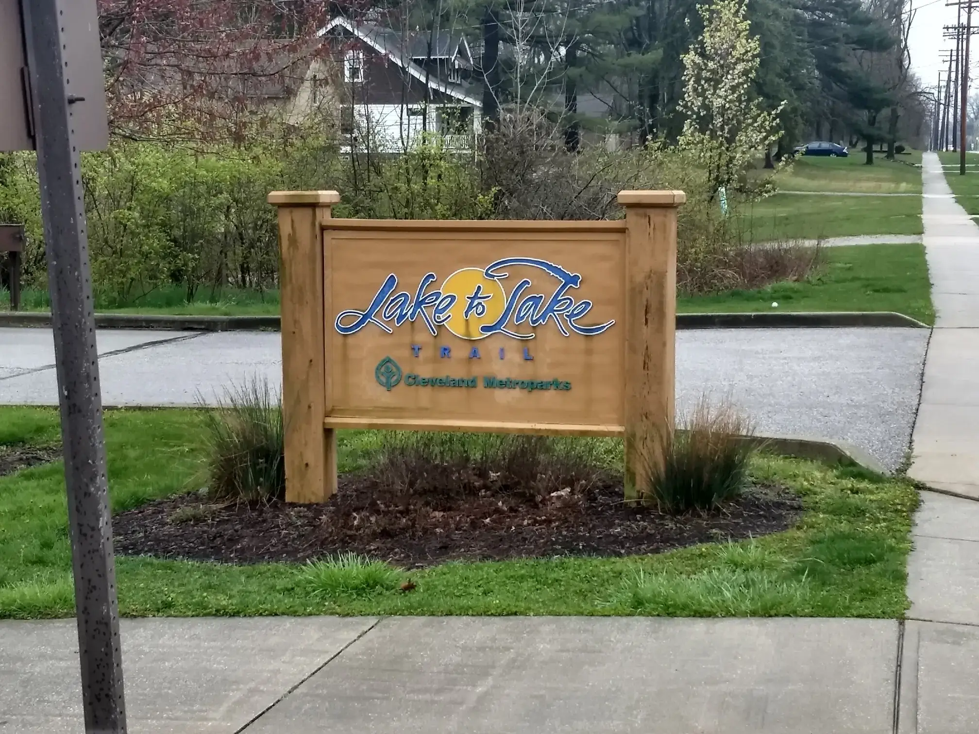 A wooden sign on a grassy median next to a paved road.