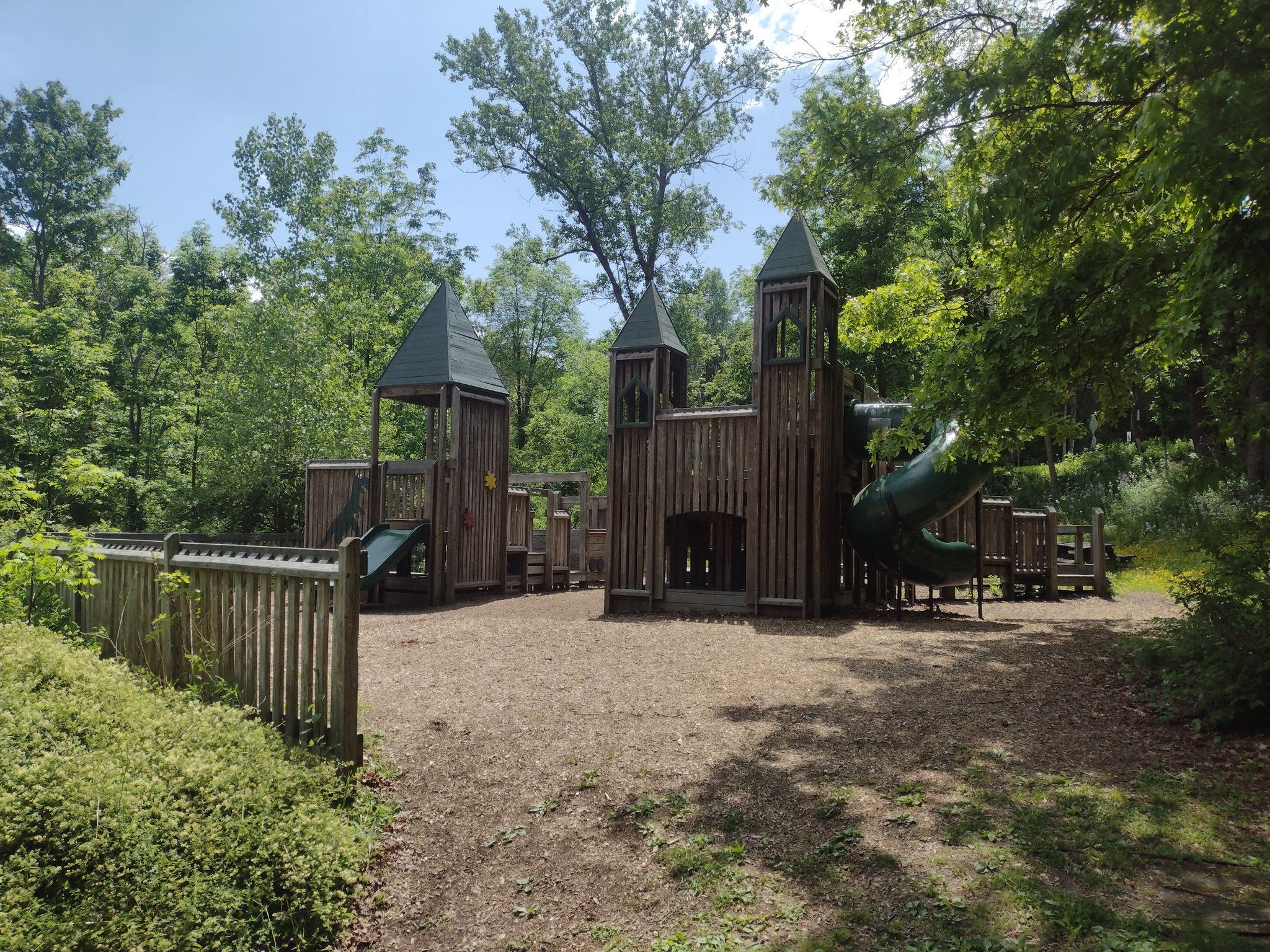 Large wooden castle-themed playground with slides, surrounded by green trees. - South Hill Recreation Way
