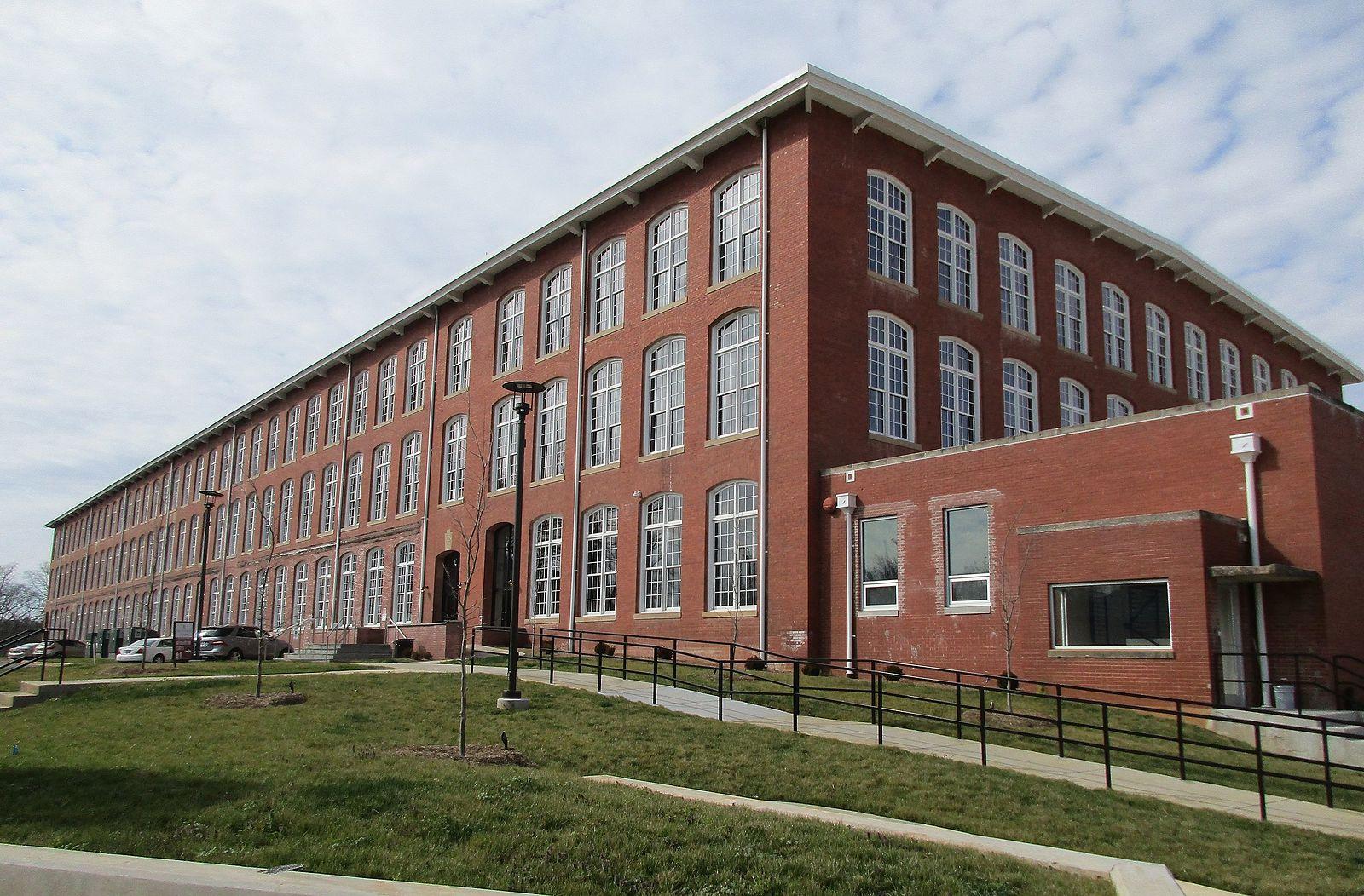 A large red brick building with many windows under a cloudy sky.
