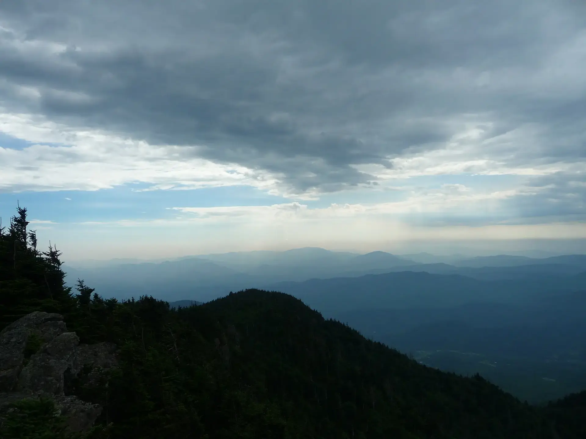 Overcast mountain landscape with silhouetted peaks and hazy distant ranges.