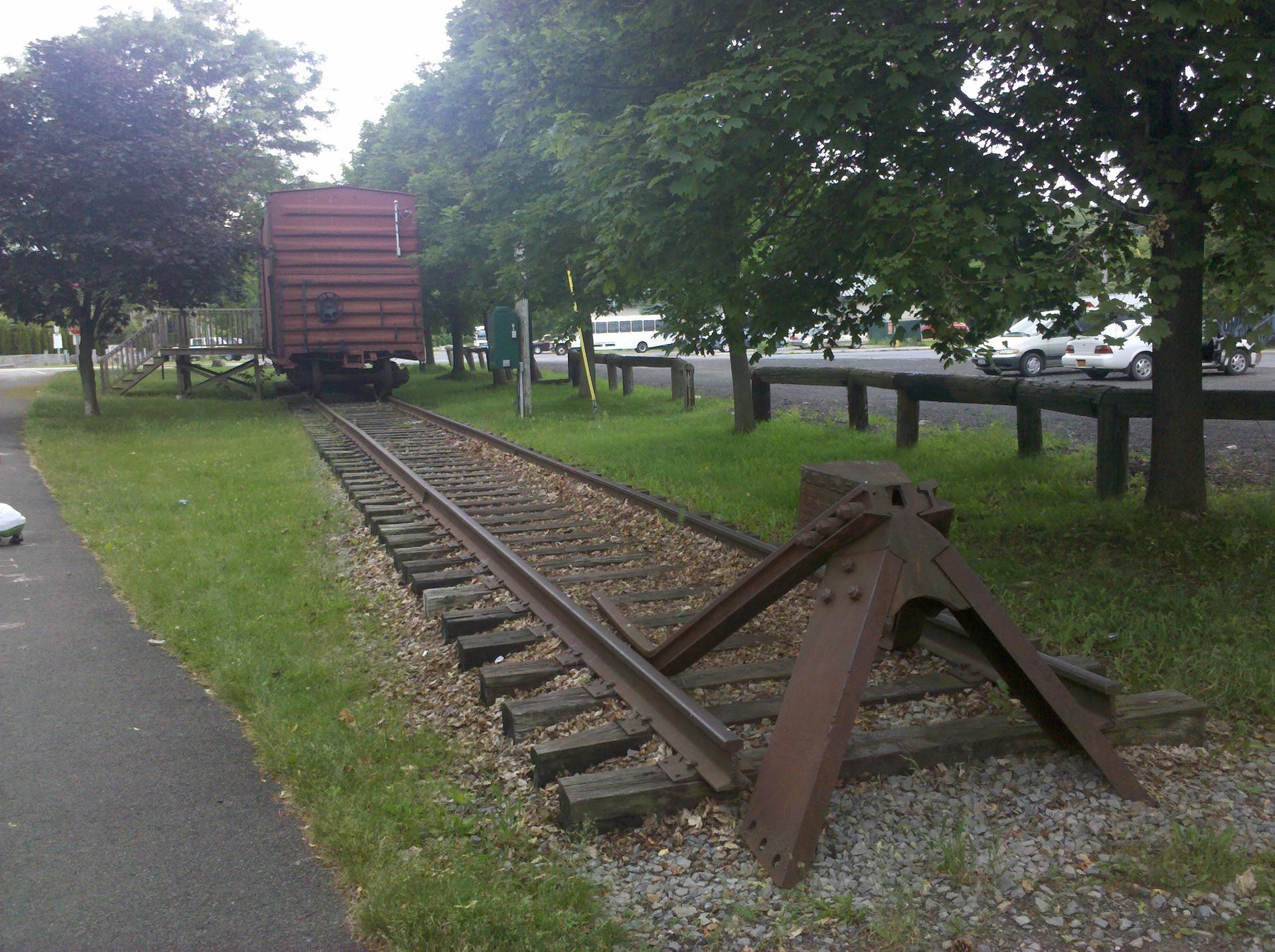 Train tracks with a buffer and a red freight car under overcast skies.