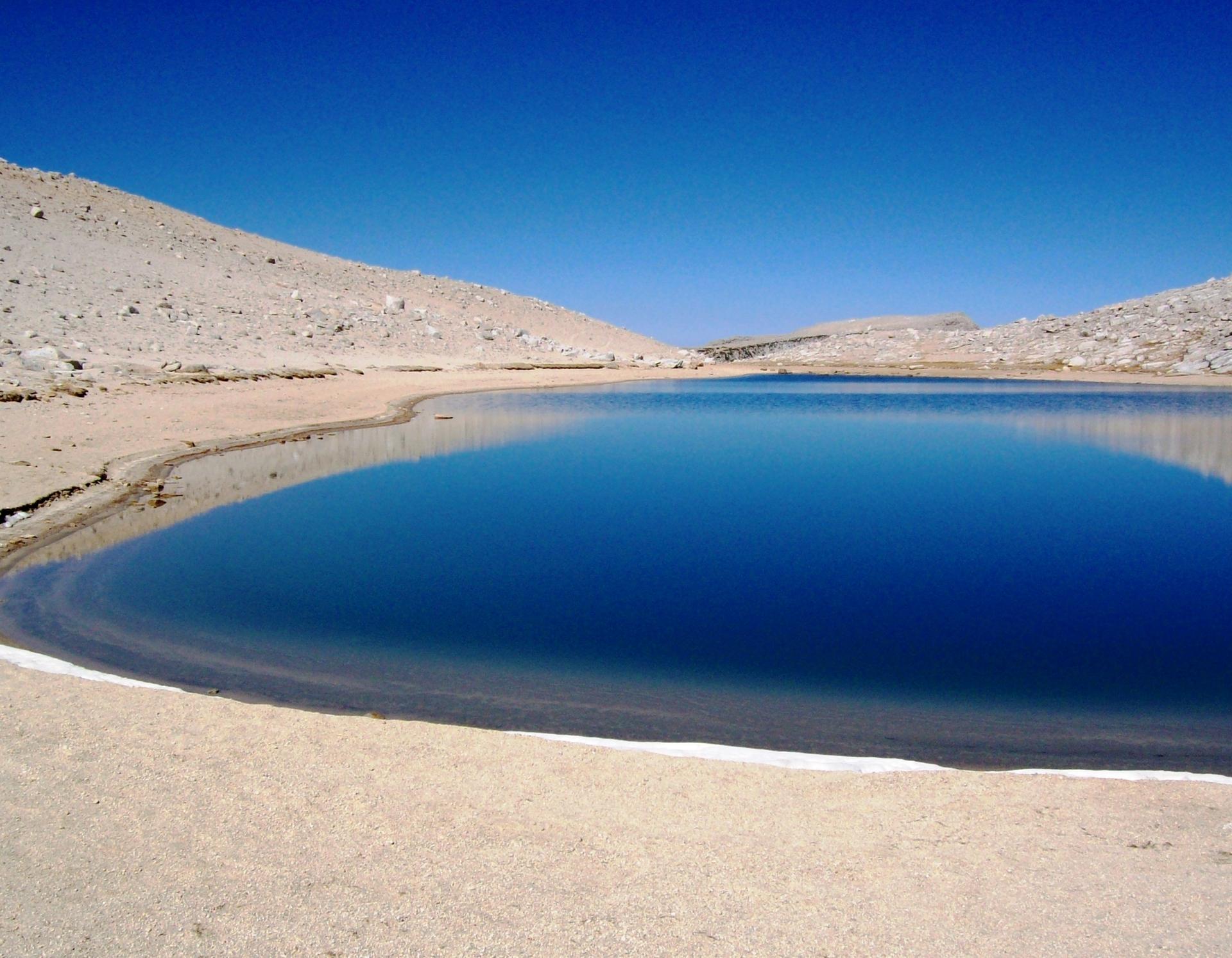 Serene blue lake with sandy shores reflecting a clear sky.