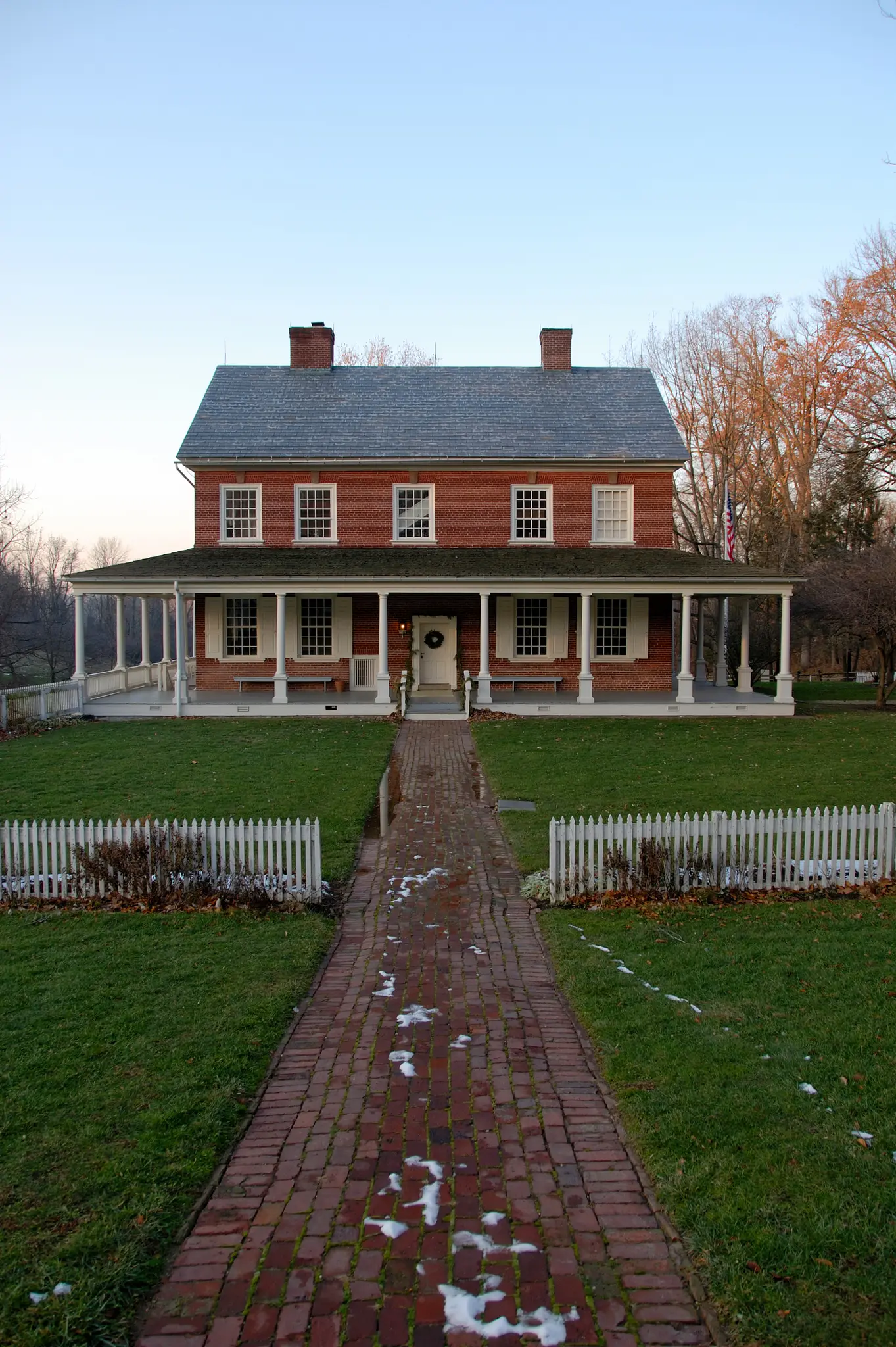 A red brick house with a white porch and fence, on a clear day.