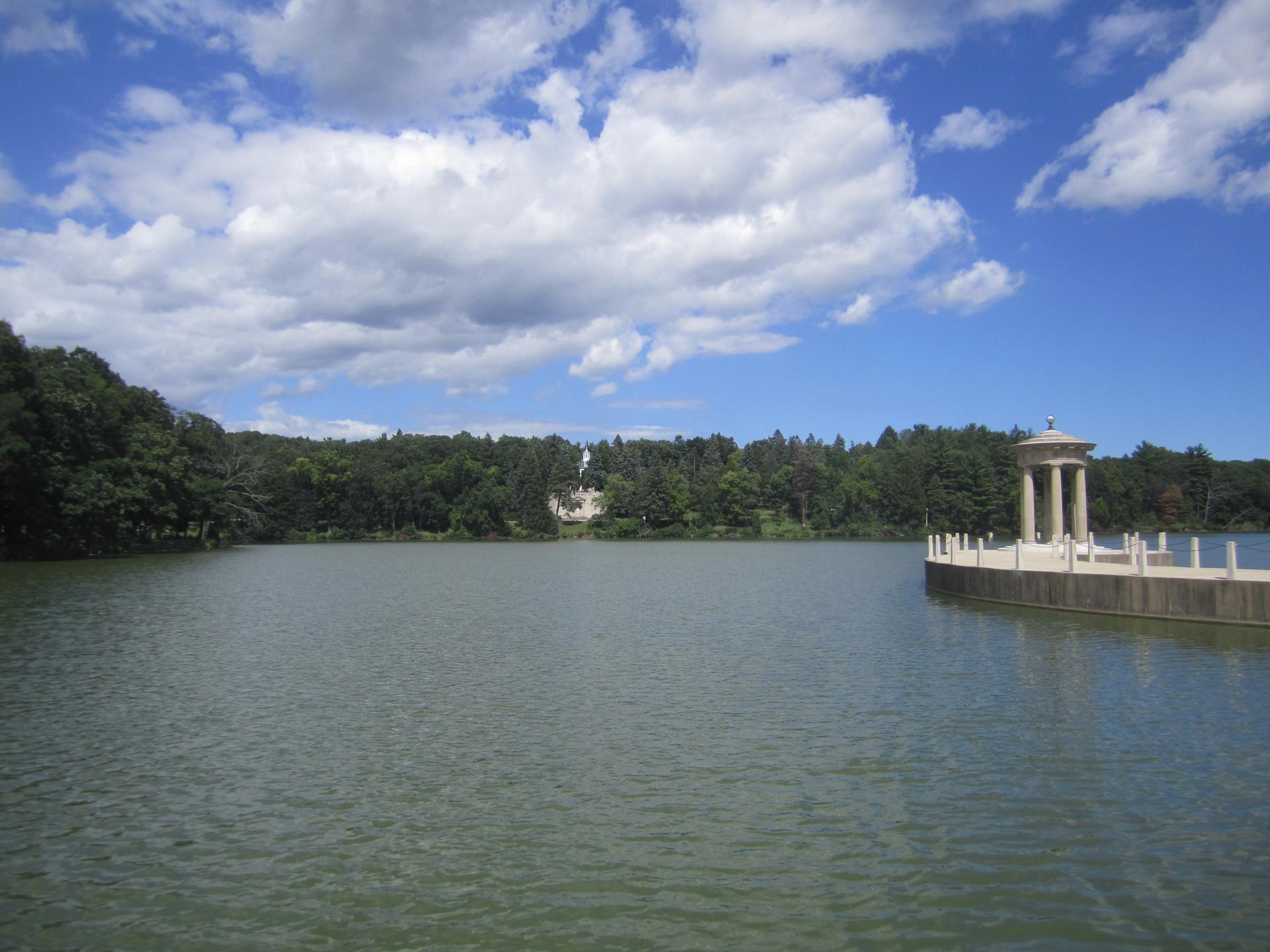 Serene lake with a classical gazebo on a dock under a bright sky.