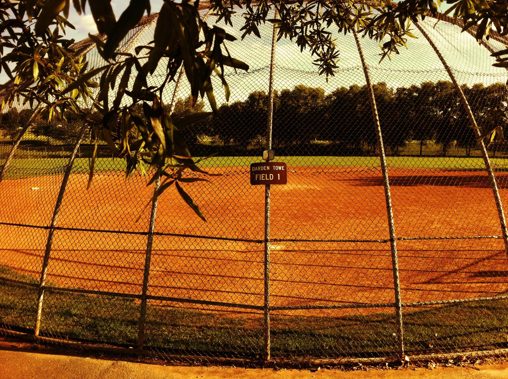 Sunny view of an empty baseball field through a chain-link fence.
