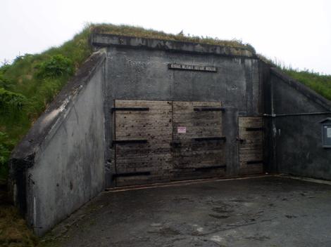 Concrete bunker with large wooden doors built into a grassy hill.