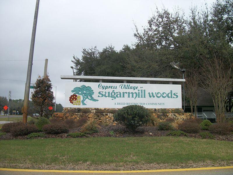 A large white sign with green text and a tree logo, surrounded by landscaping.