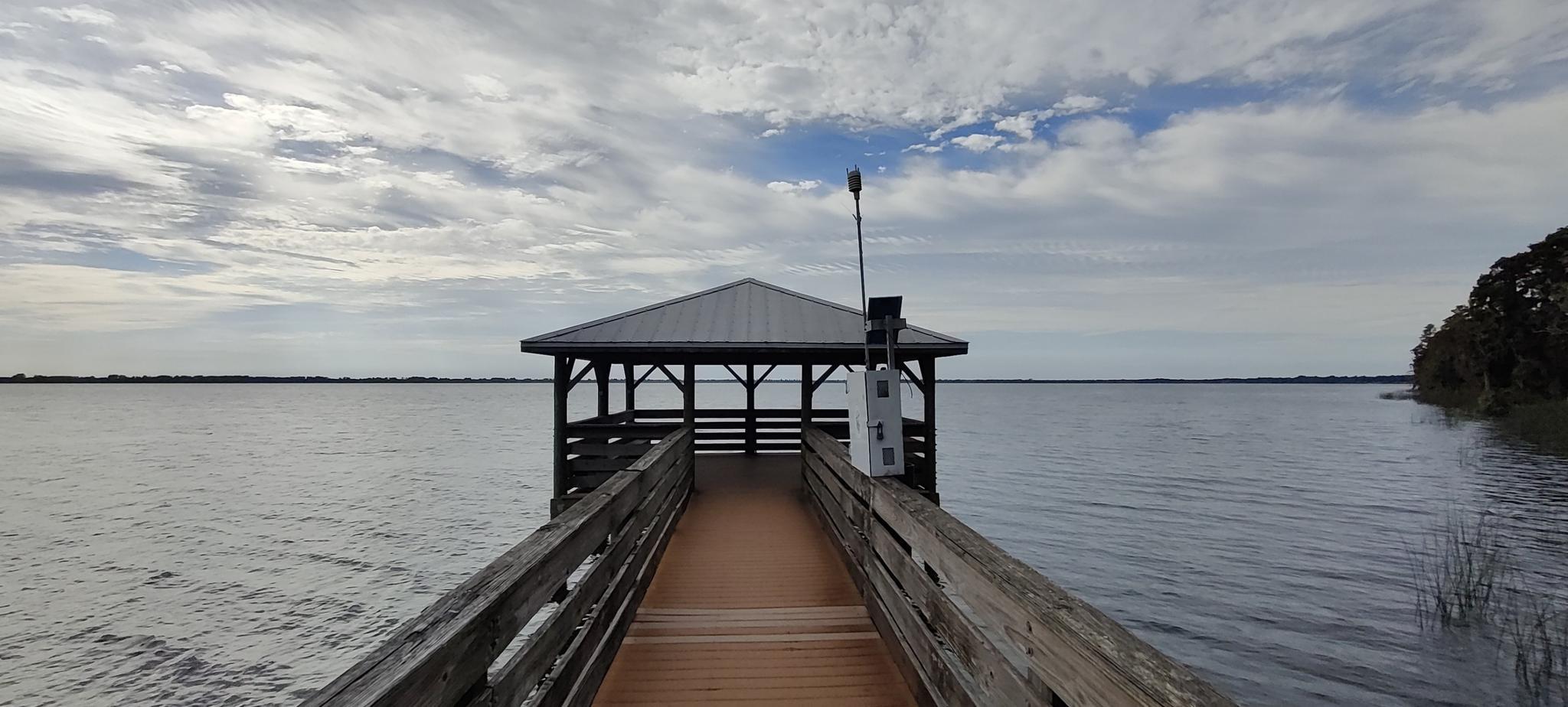 A wooden pier extends to a covered gazebo over a wide, calm lake.