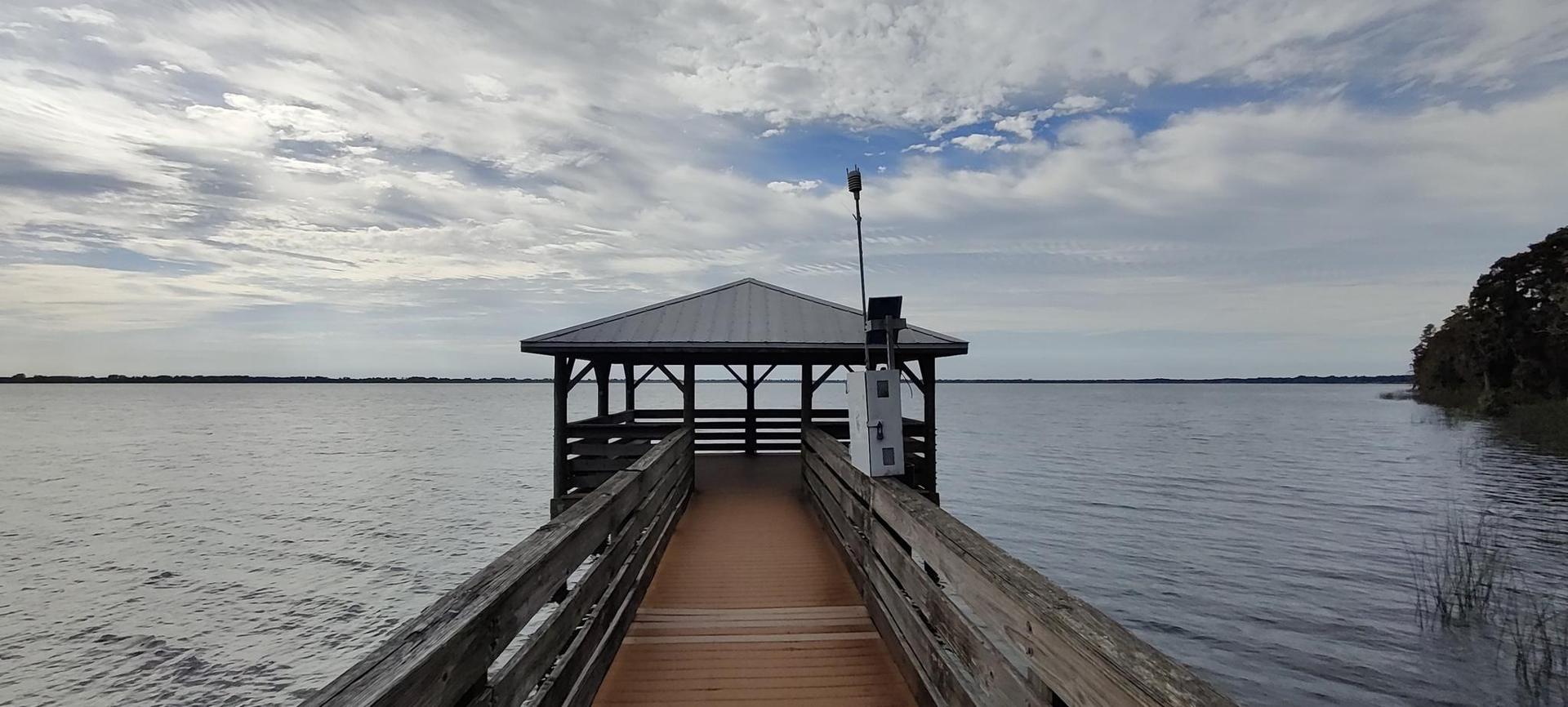 A wooden pier extends to a covered gazebo over a wide, calm lake.