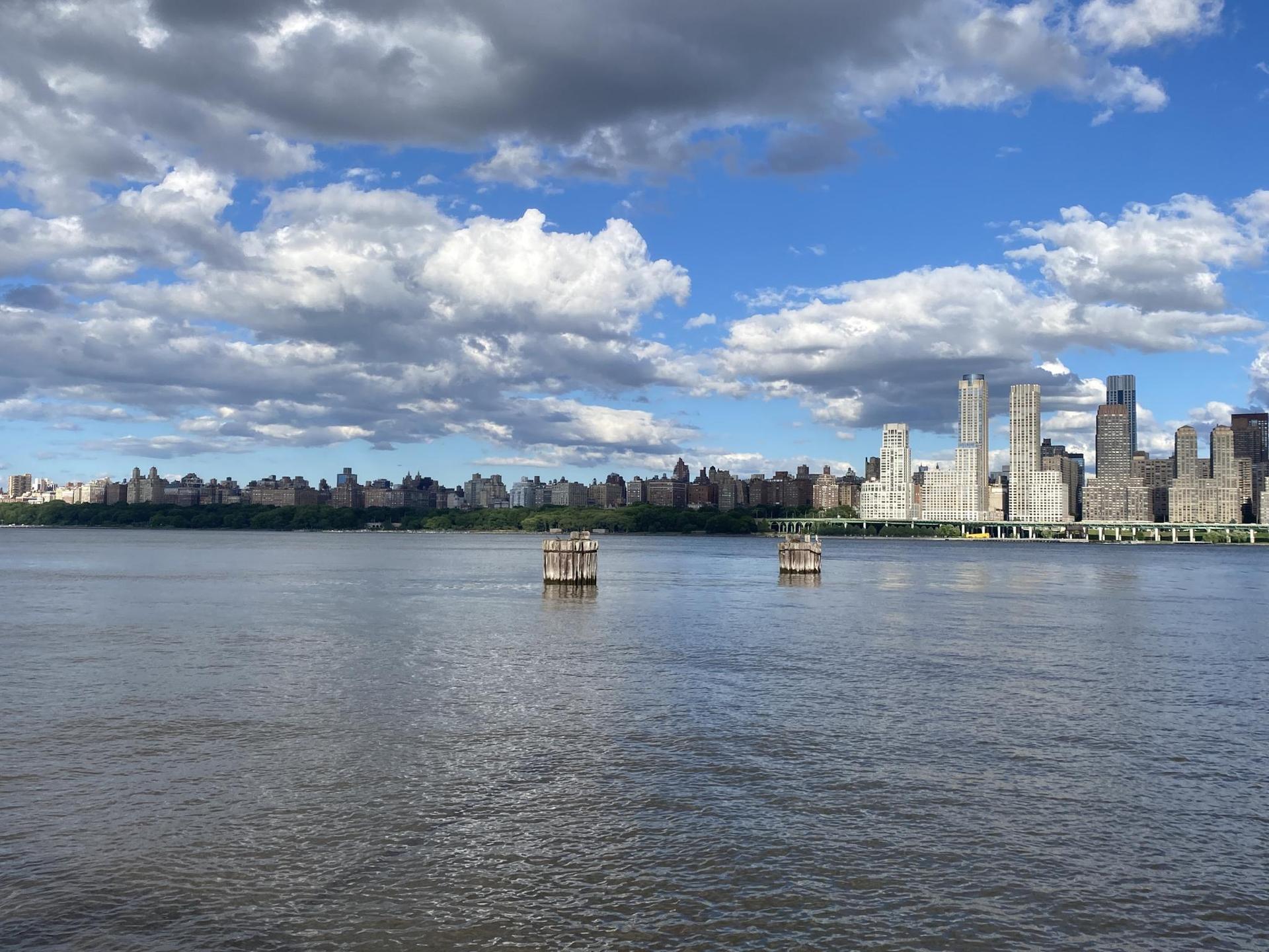 Wide river with distant city skyline under a cloudy blue sky.