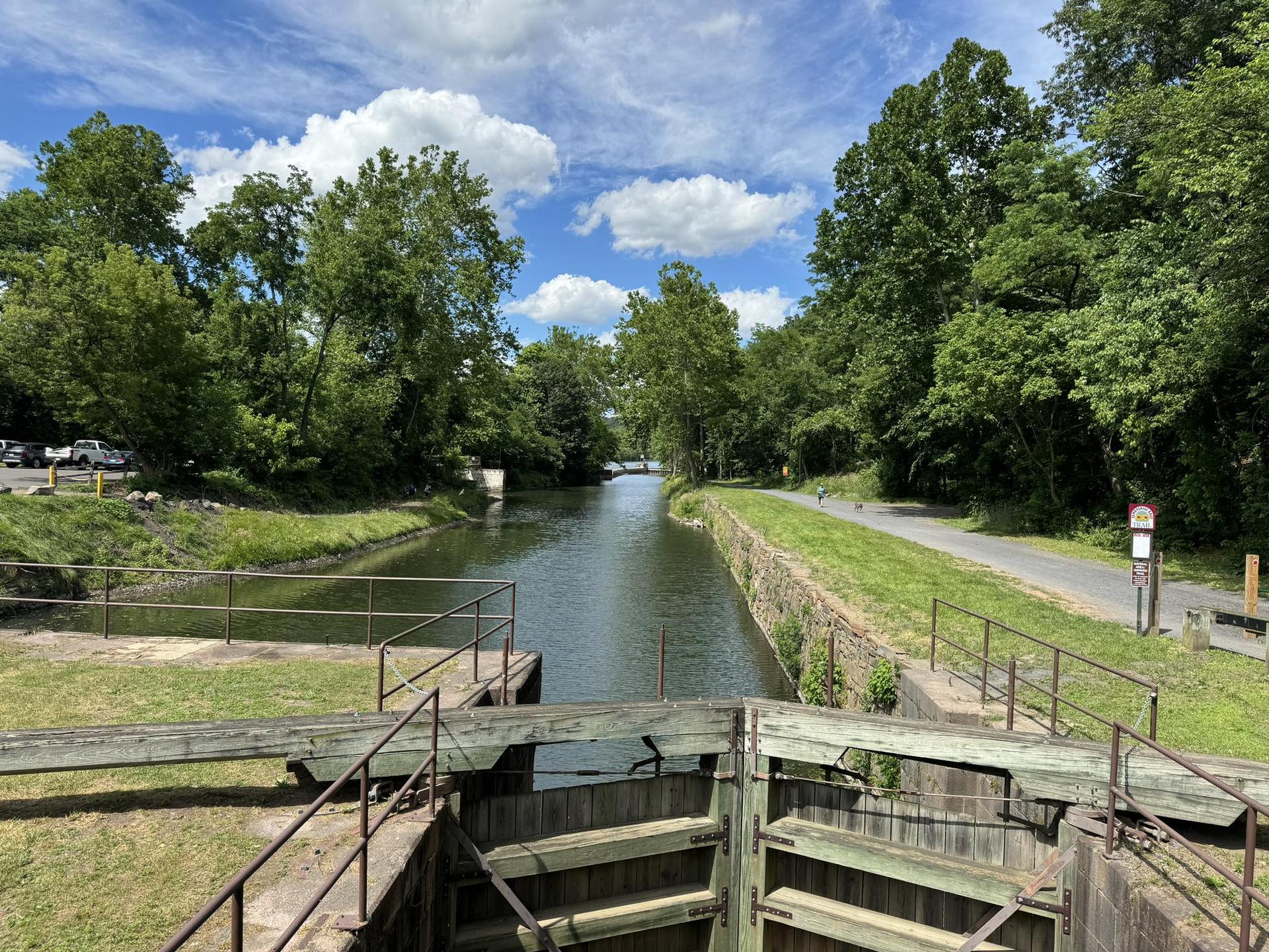 Canal lock with open gates, surrounded by lush green trees under a blue sky.