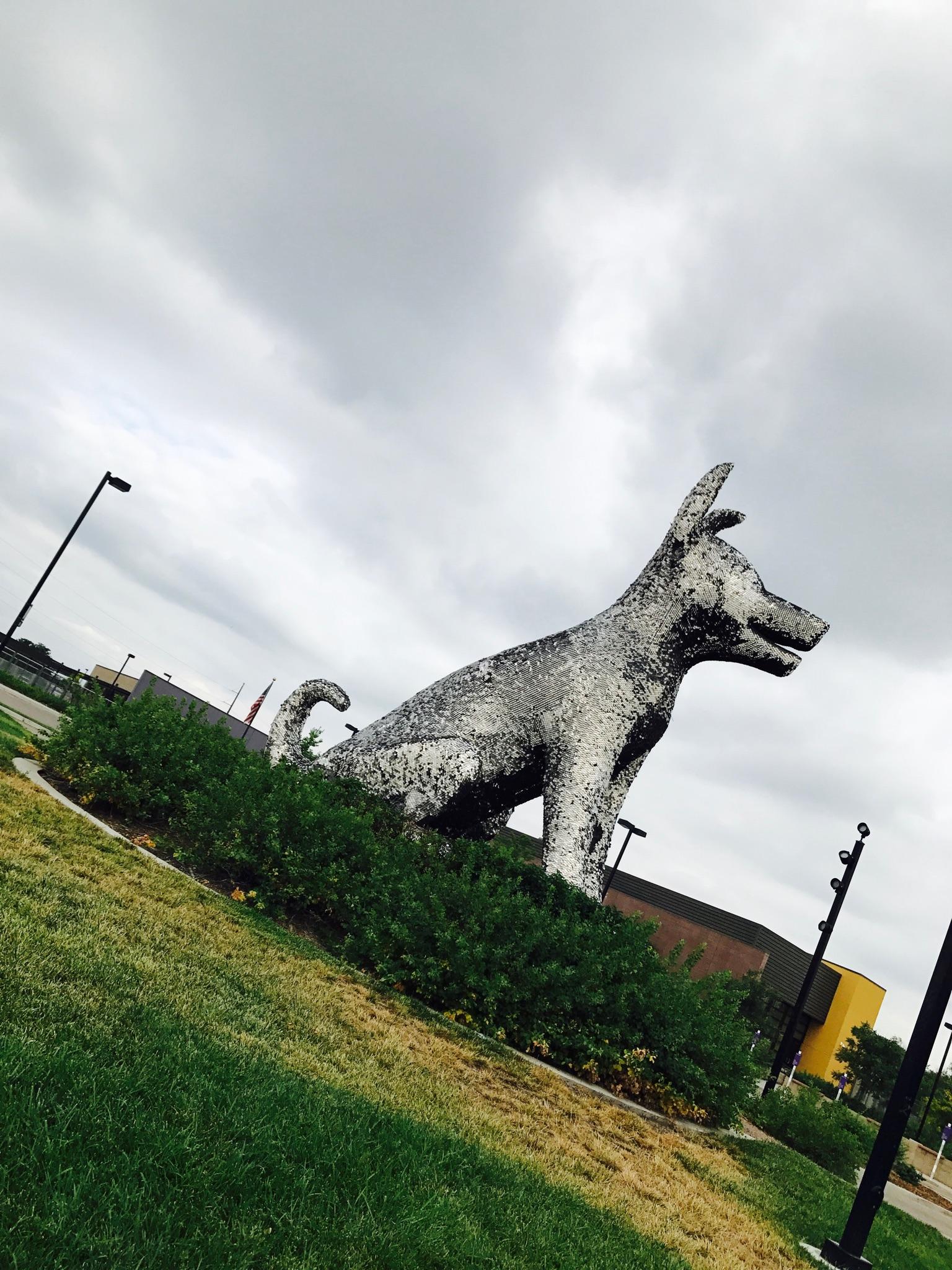 Large, textured dog sculpture in a grassy area under a cloudy sky.