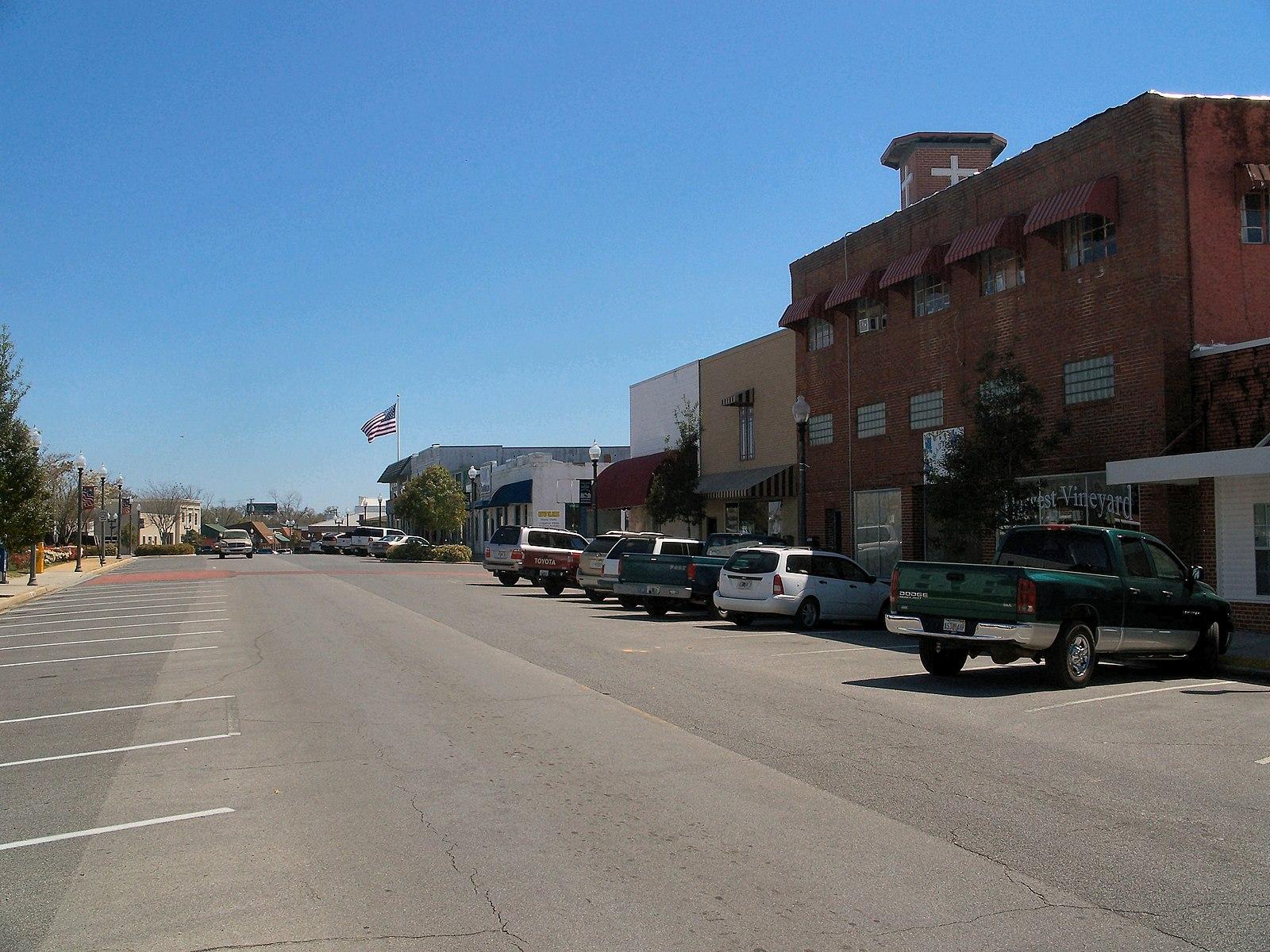 Sunny street scene with parked cars and brick buildings.