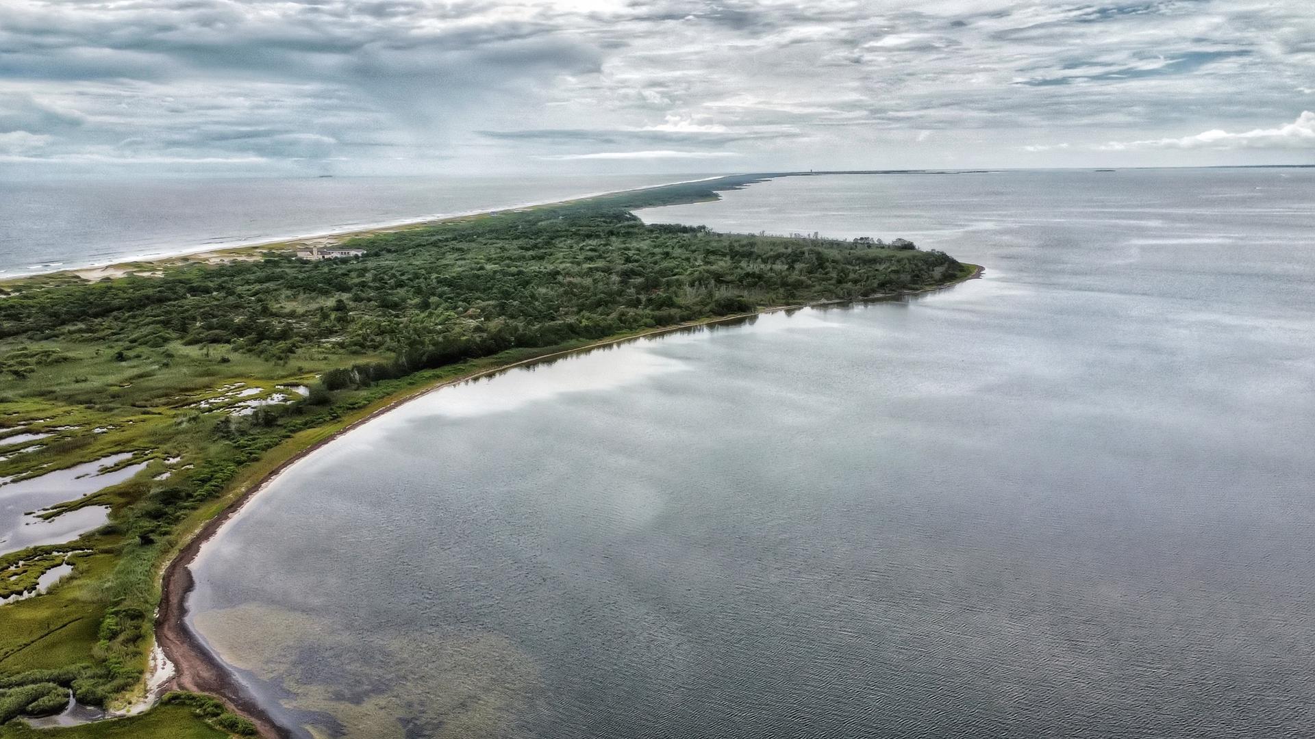 Aerial view of a long, green landmass surrounded by calm water under cloudy skies.