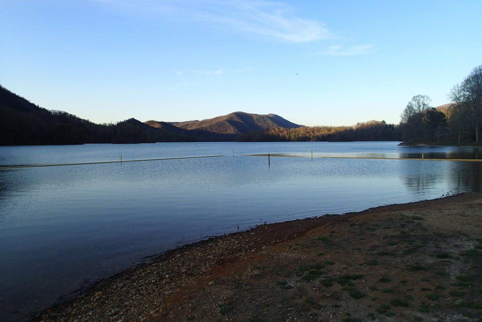 Vast lake with a buoy line, framed by dark mountains and clear sky.