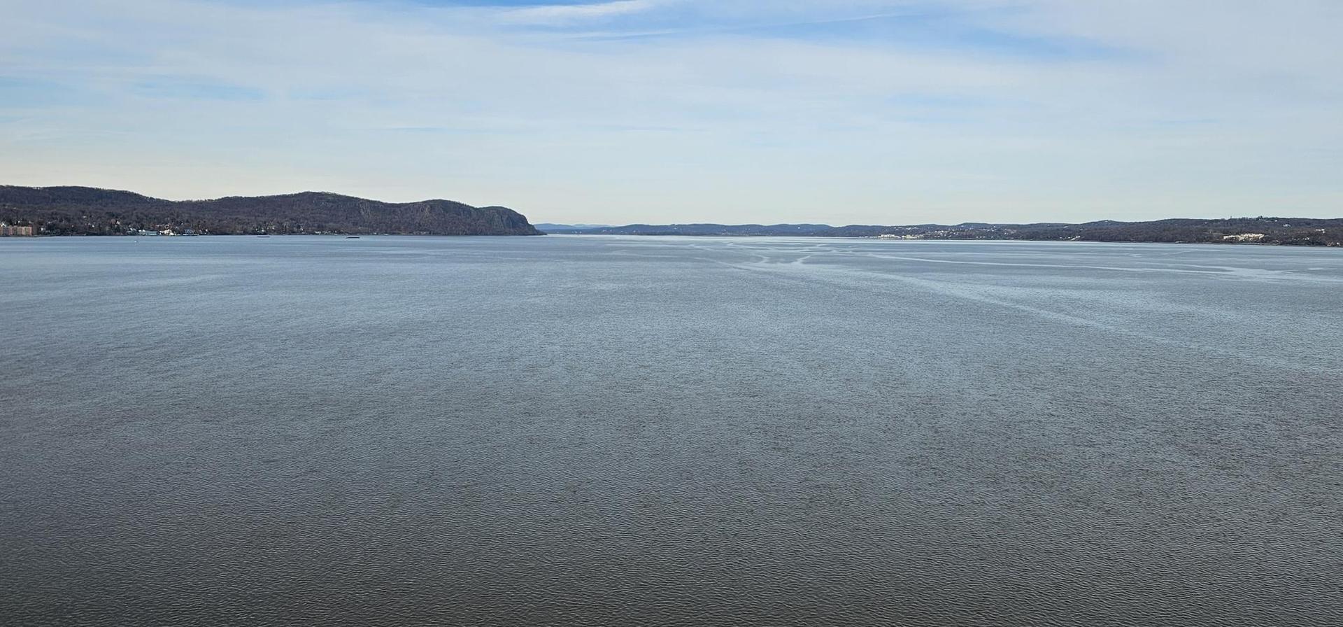 Wide expanse of calm water with distant hills under a partly cloudy sky.