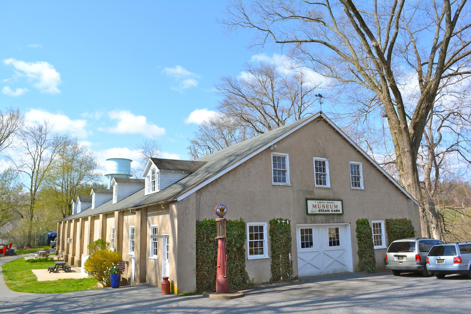 A long, tan museum building with dormers and bare trees under a sunny sky.