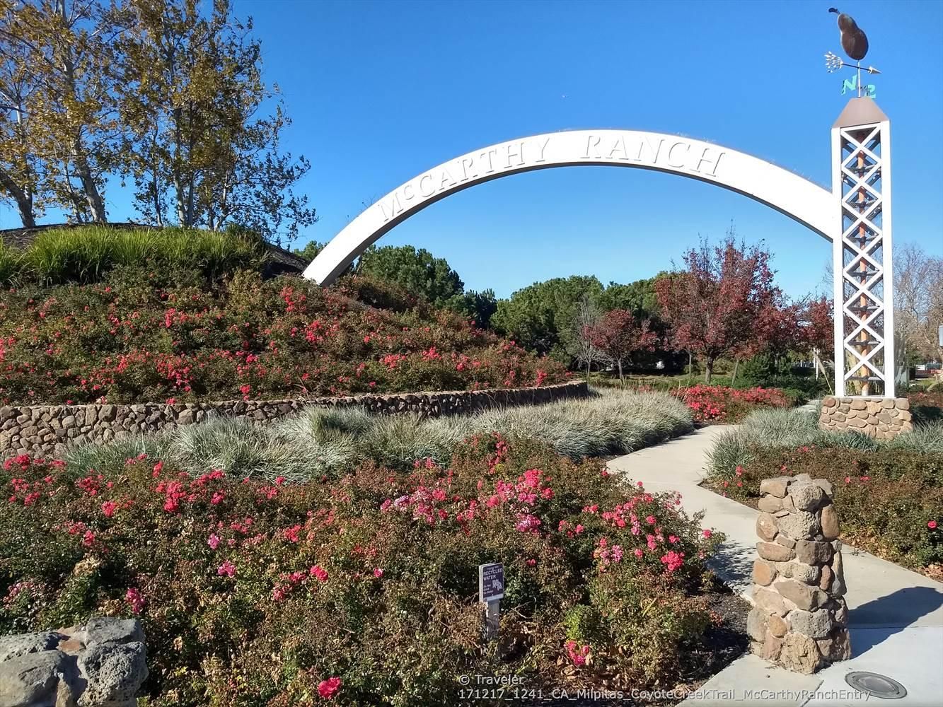 White arched sign and tower with weathervane, colorful bushes, sunny day. - Coyote Creek Trail