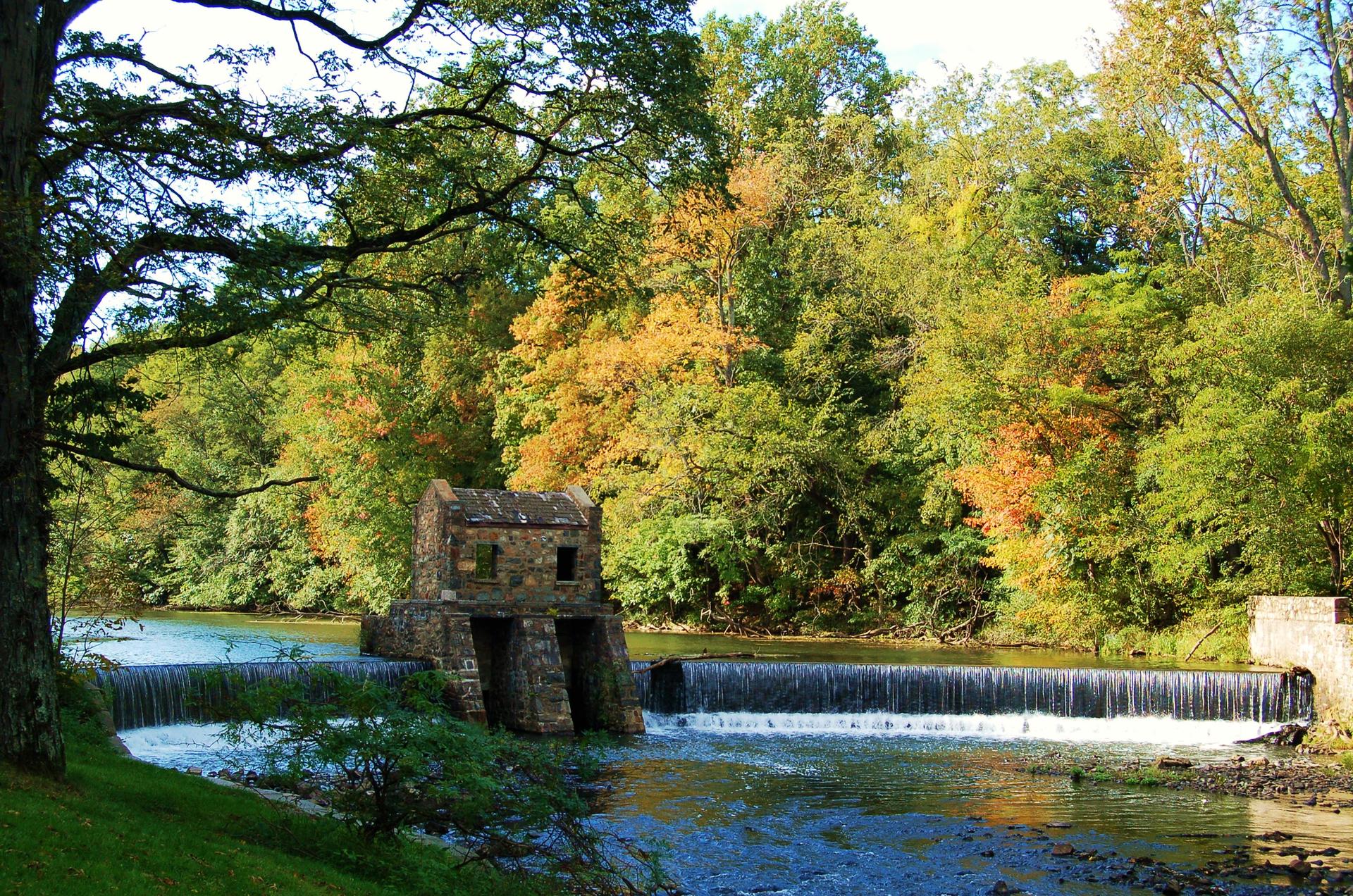 Historic stone building and waterfall on a river with autumn trees.