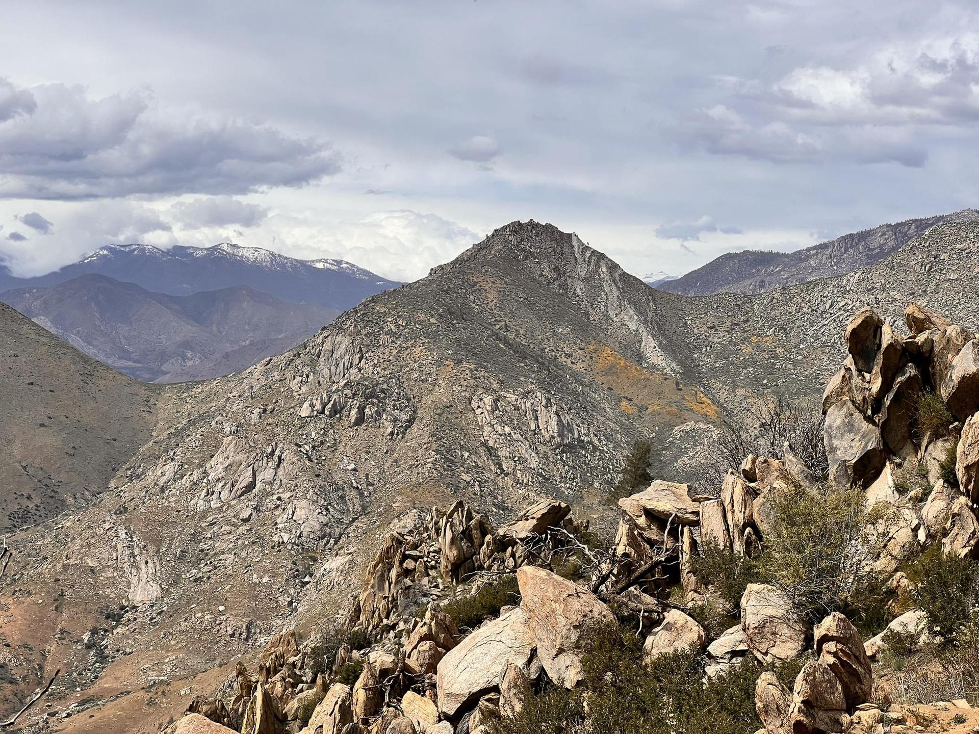 Rocky mountain landscape under a cloudy sky, with distant snow-capped peaks.