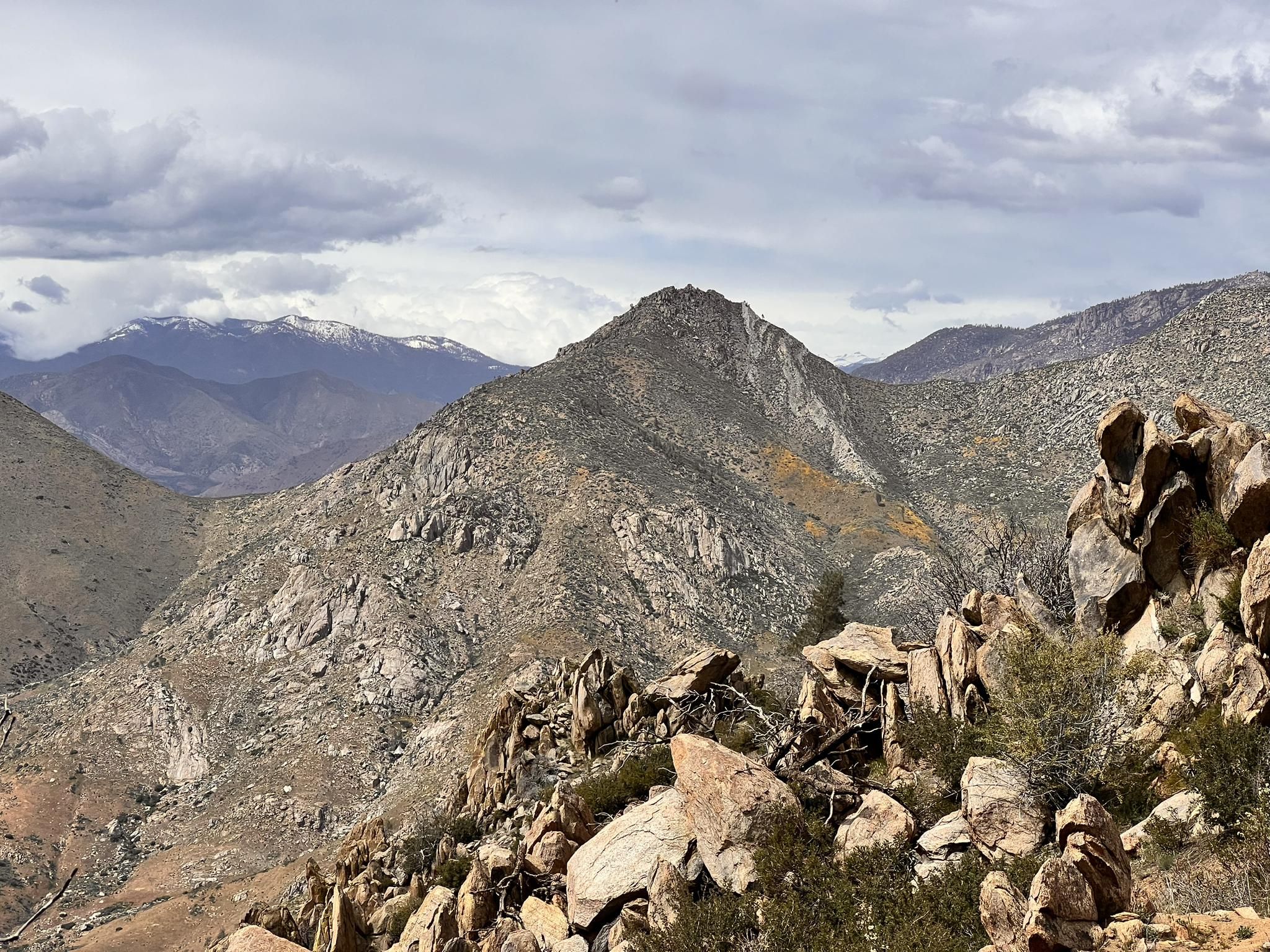 Rocky mountain landscape under a cloudy sky, with distant snow-capped peaks. - Powers Peak