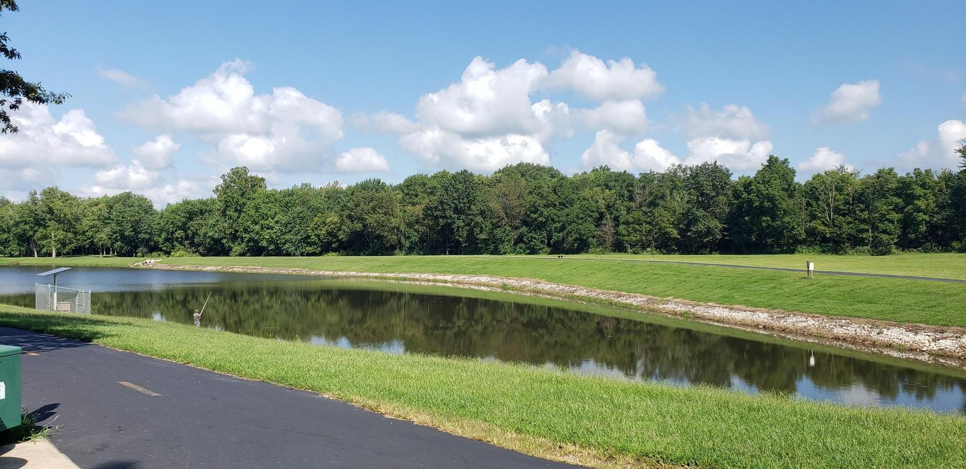 A long pond with grassy banks, a paved path, and distant trees.